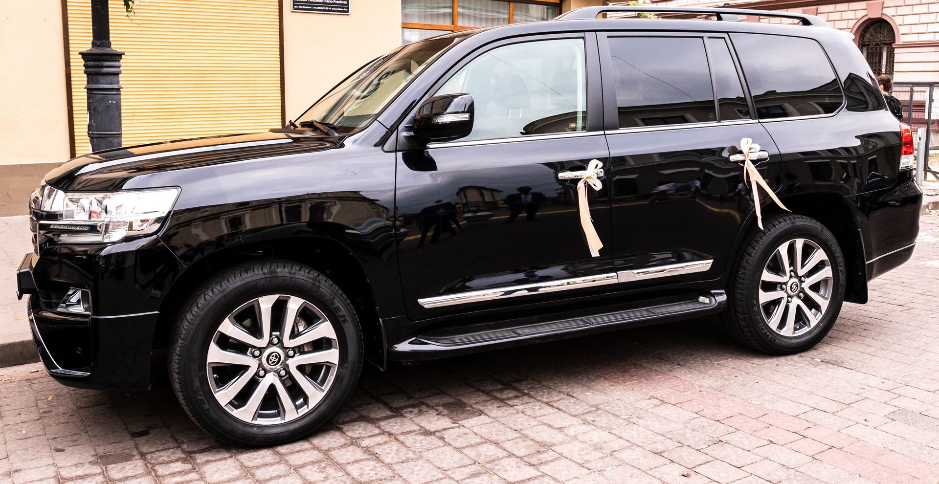 Black SUV parked on a brick driveway beside a yellow building.