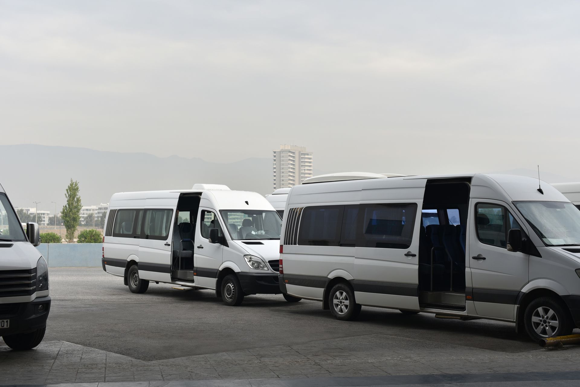 Three white minibuses parked in a lot, one with its sliding door open under a cloudy sky