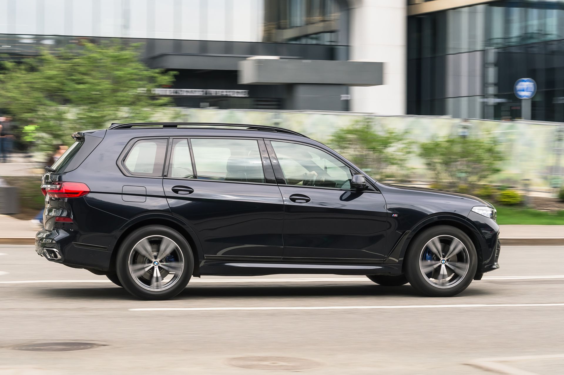 Black SUV driving on a city street with blurred background greenery and buildings
