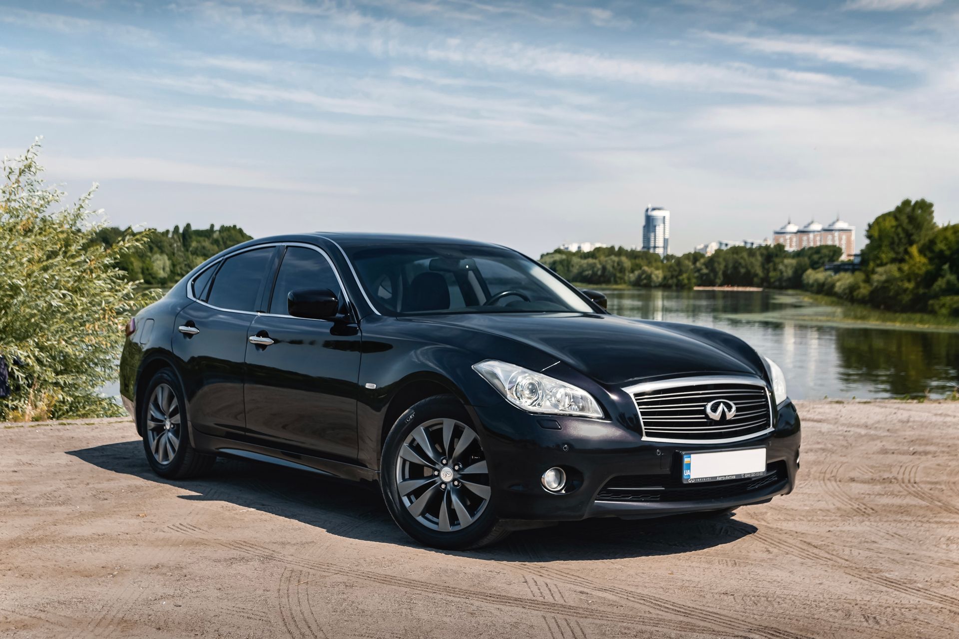 Black sedan parked by a lakeside road under a clear sky.