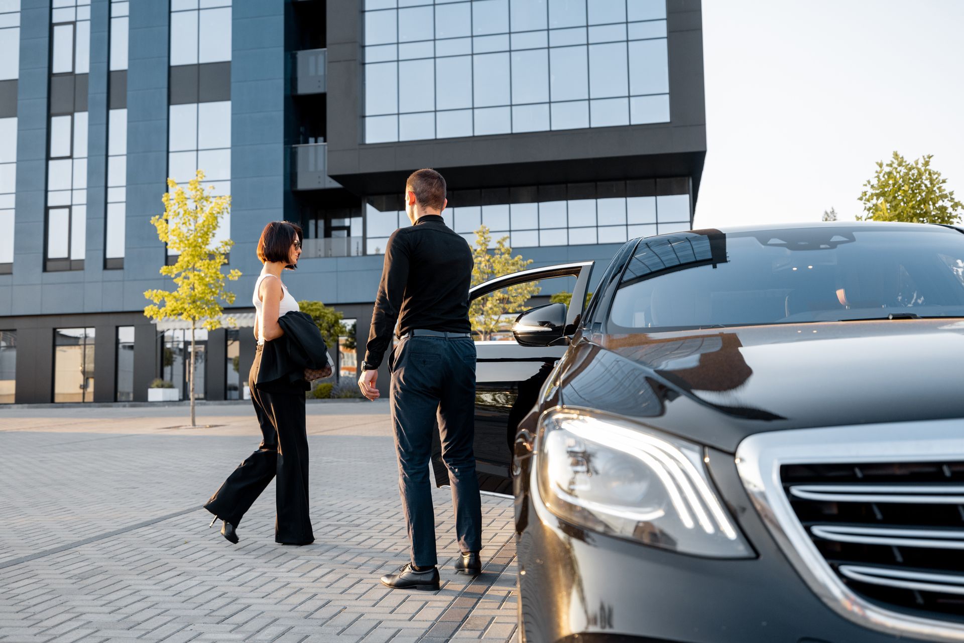 Two people walking beside a black car outside a modern office building