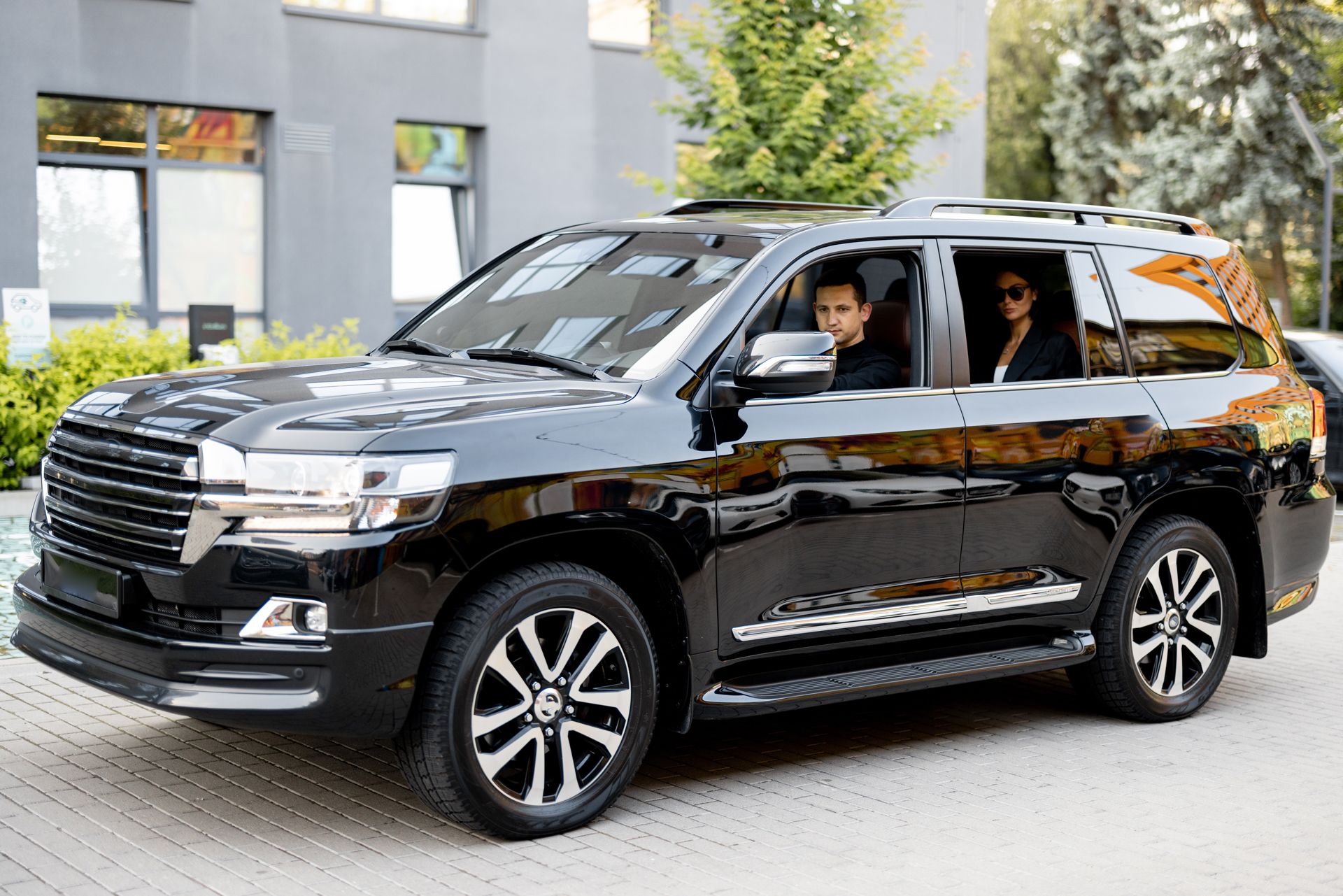 Black SUV with two people inside parked outside a modern building