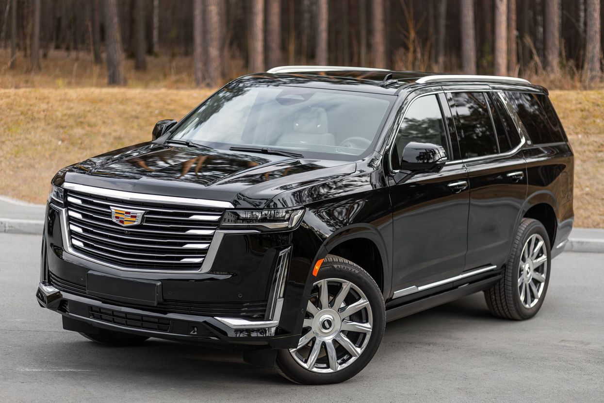 Black Cadillac SUV parked on a road in a wooded area