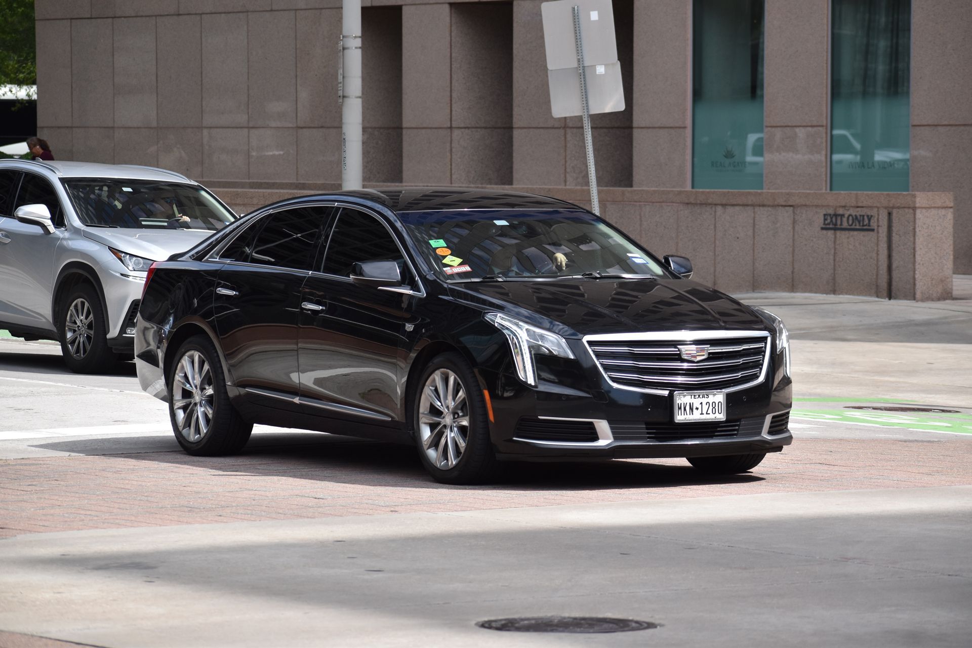 Black sedan driving on a city street beside a white SUV, near a building.