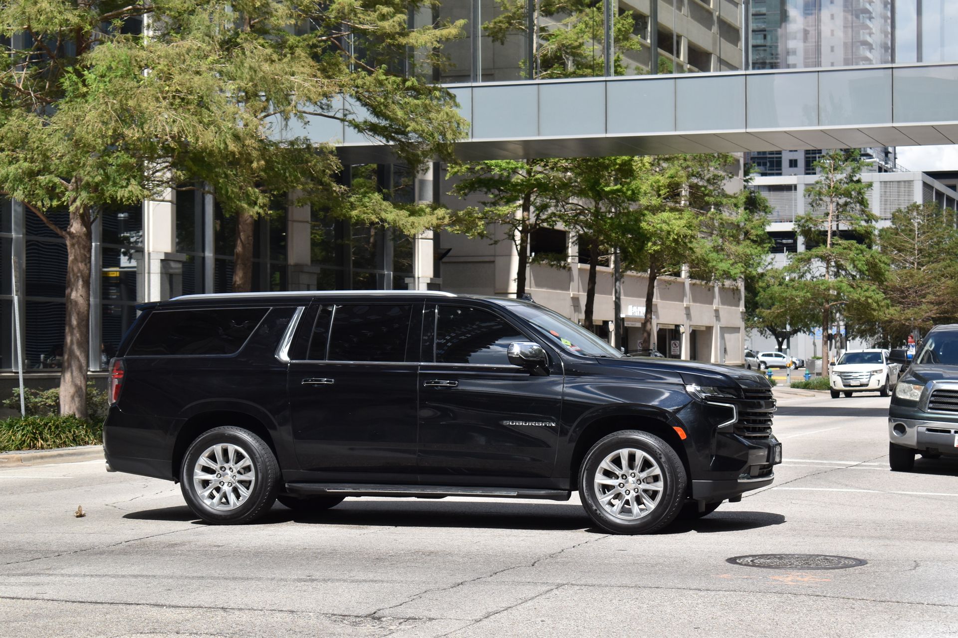 Black SUV driving through a city street near modern buildings and trees.
