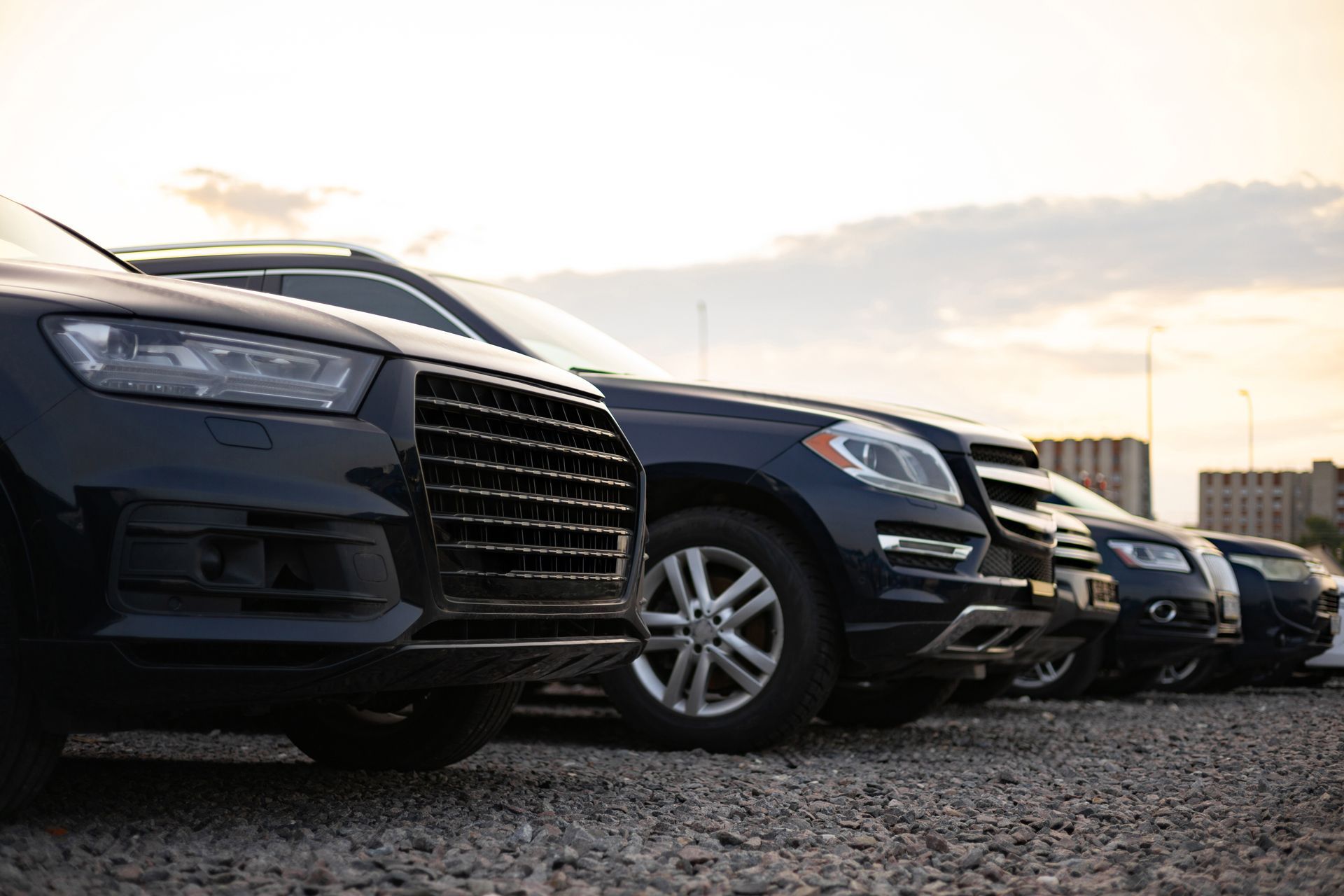 Row of parked dark SUVs on a gravel lot at sunset