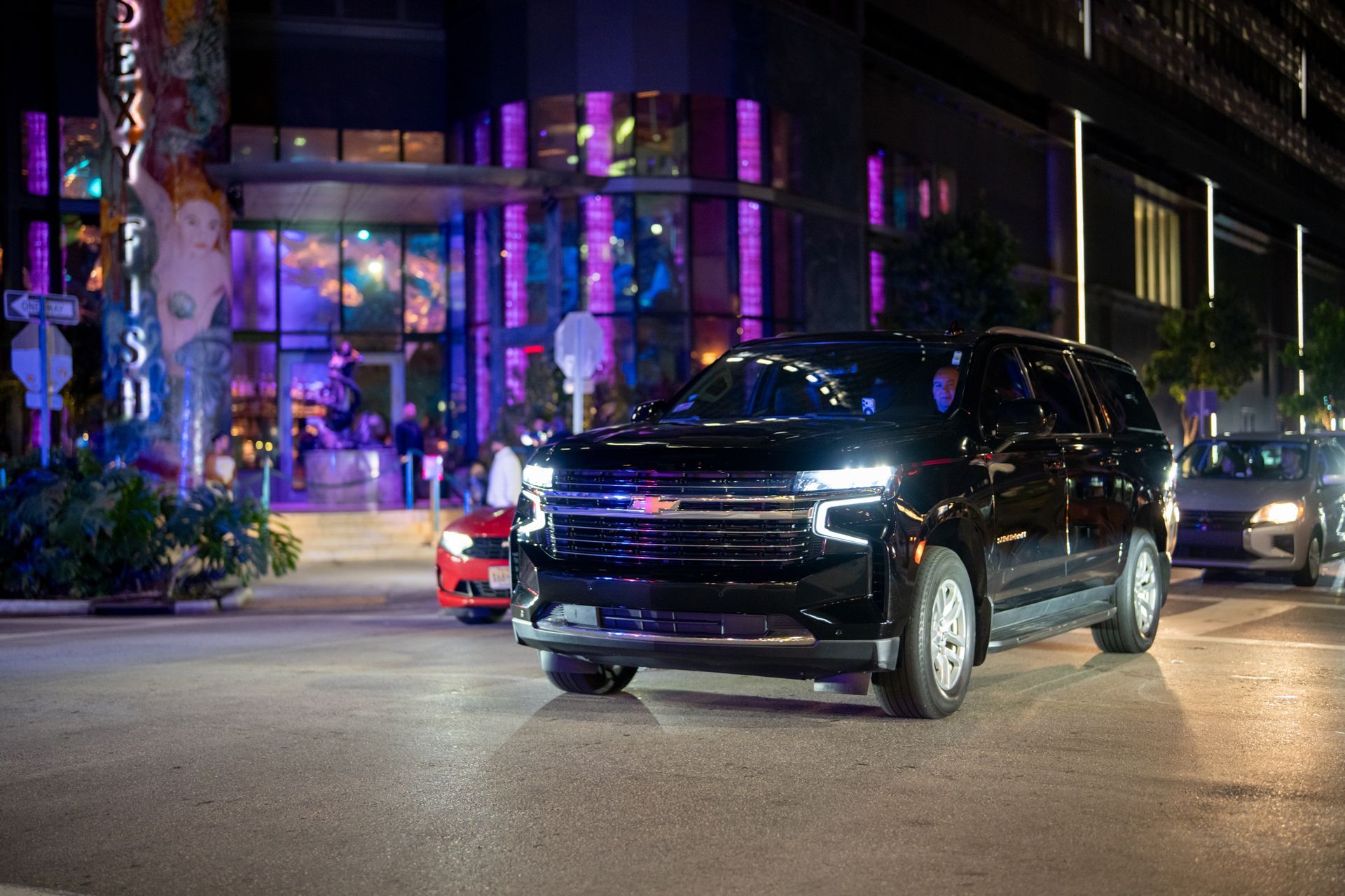 Black SUV driving on a city street at night with colorful neon-lit buildings in the background
