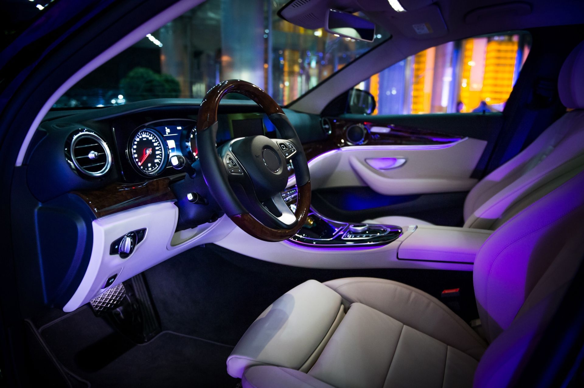 Luxury car interior lit with purple ambient lights, beige seats, and illuminated dashboard at night