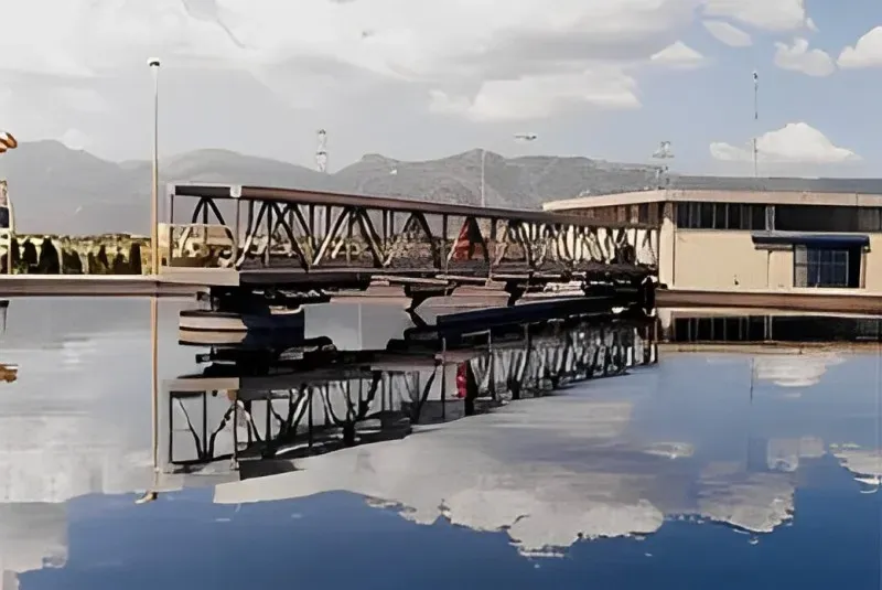 Attrezzature industriali che si estendono sull'acqua, riflettendo il cielo e le montagne.