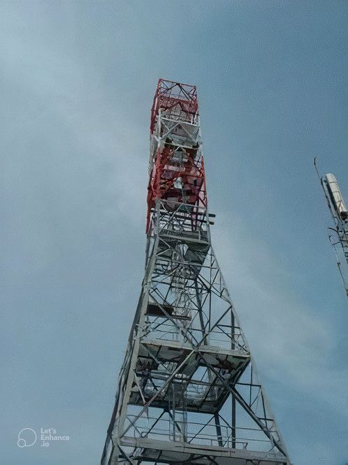 Torre di comunicazione in acciaio contro un cielo azzurro nuvoloso, la parte superiore dipinta di rosso e bianco.