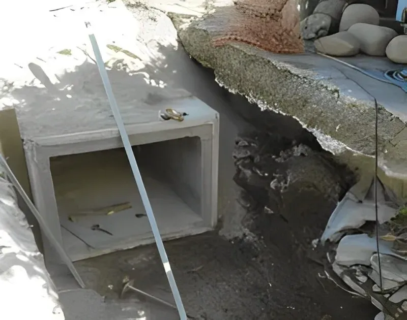 Condotto di drenaggio rettangolare in cemento installato in un fosso, con materiali da costruzione nelle vicinanze.