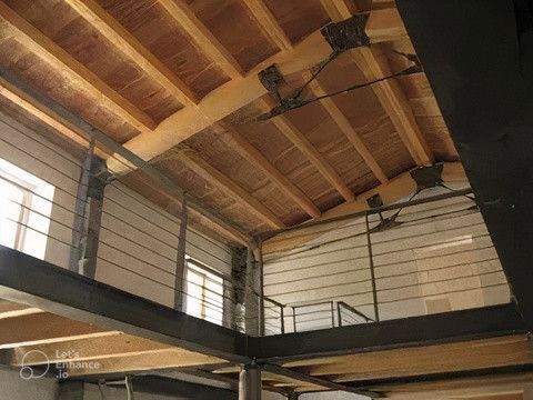 Vista interna: soffitto in legno con travi e supporti metallici, passerella al secondo piano con ringhiere in acciaio.