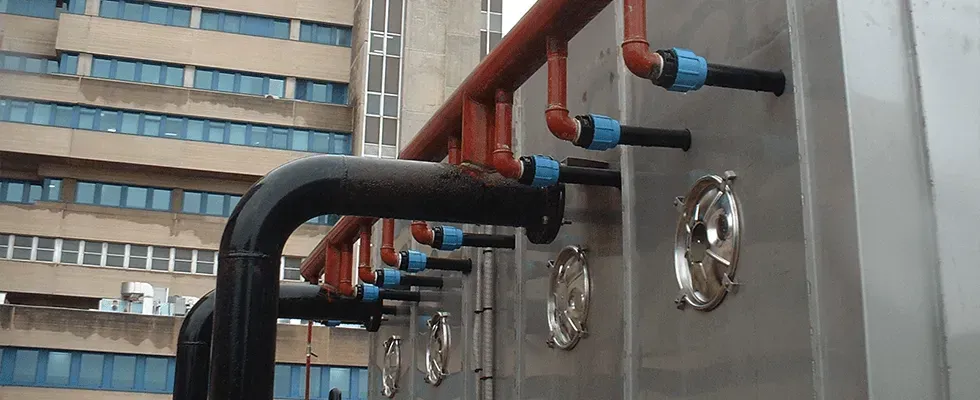 Tubazioni sulla facciata esterna di un edificio, con tubi rossi e neri, connettori blu e coperture metalliche lucide.