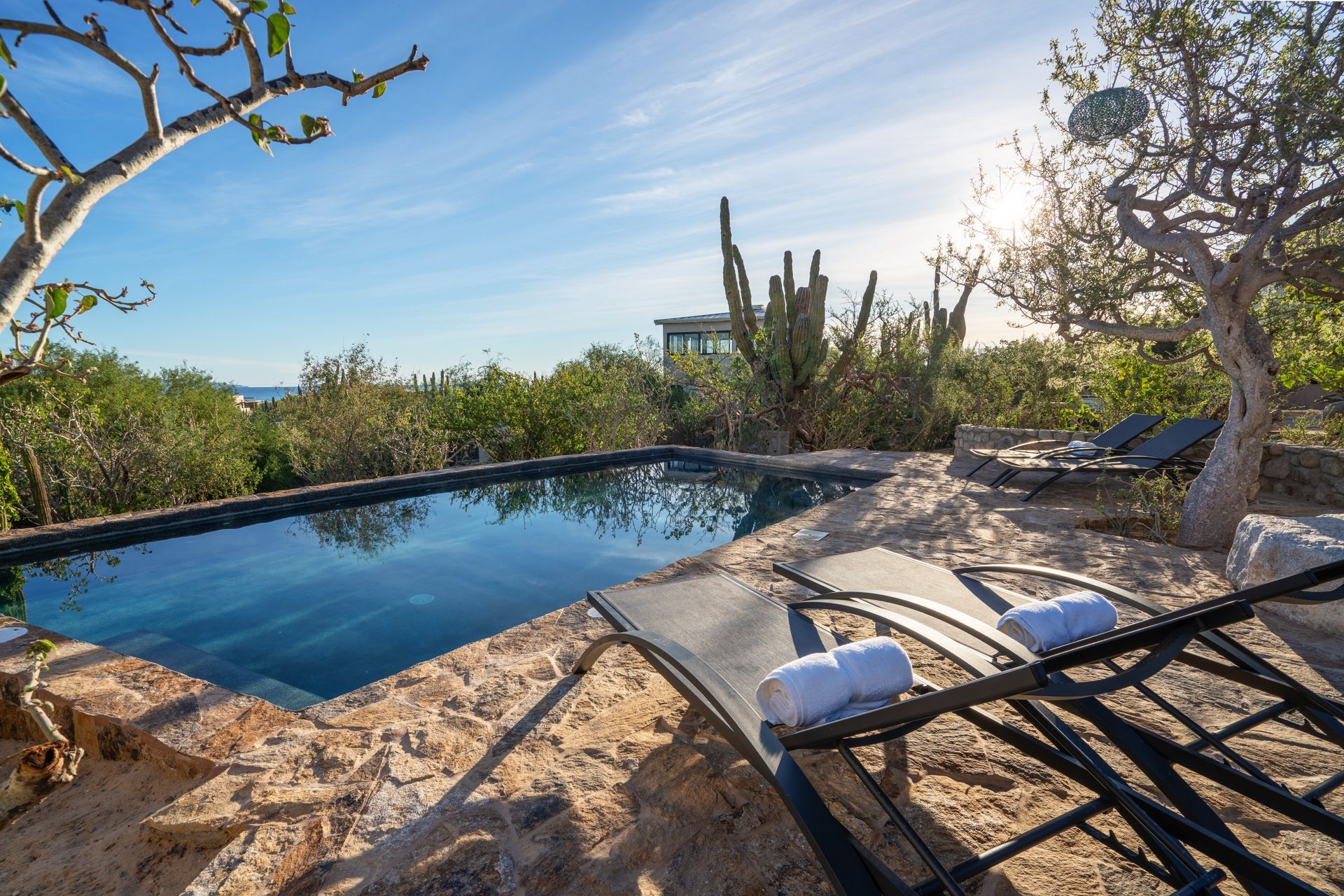 A private swimming pool with stone decking, two lounge chairs with white towels, and surrounding trees under a sunny sky.