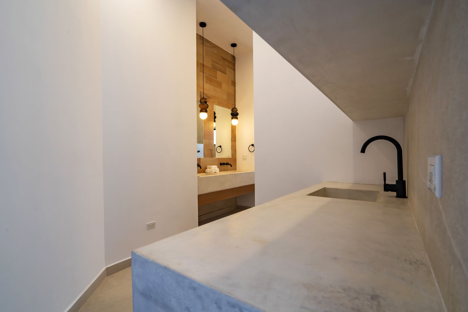 Minimalist room with a concrete countertop, black faucet, and an adjacent bathroom featuring a wooden wall and vanity.