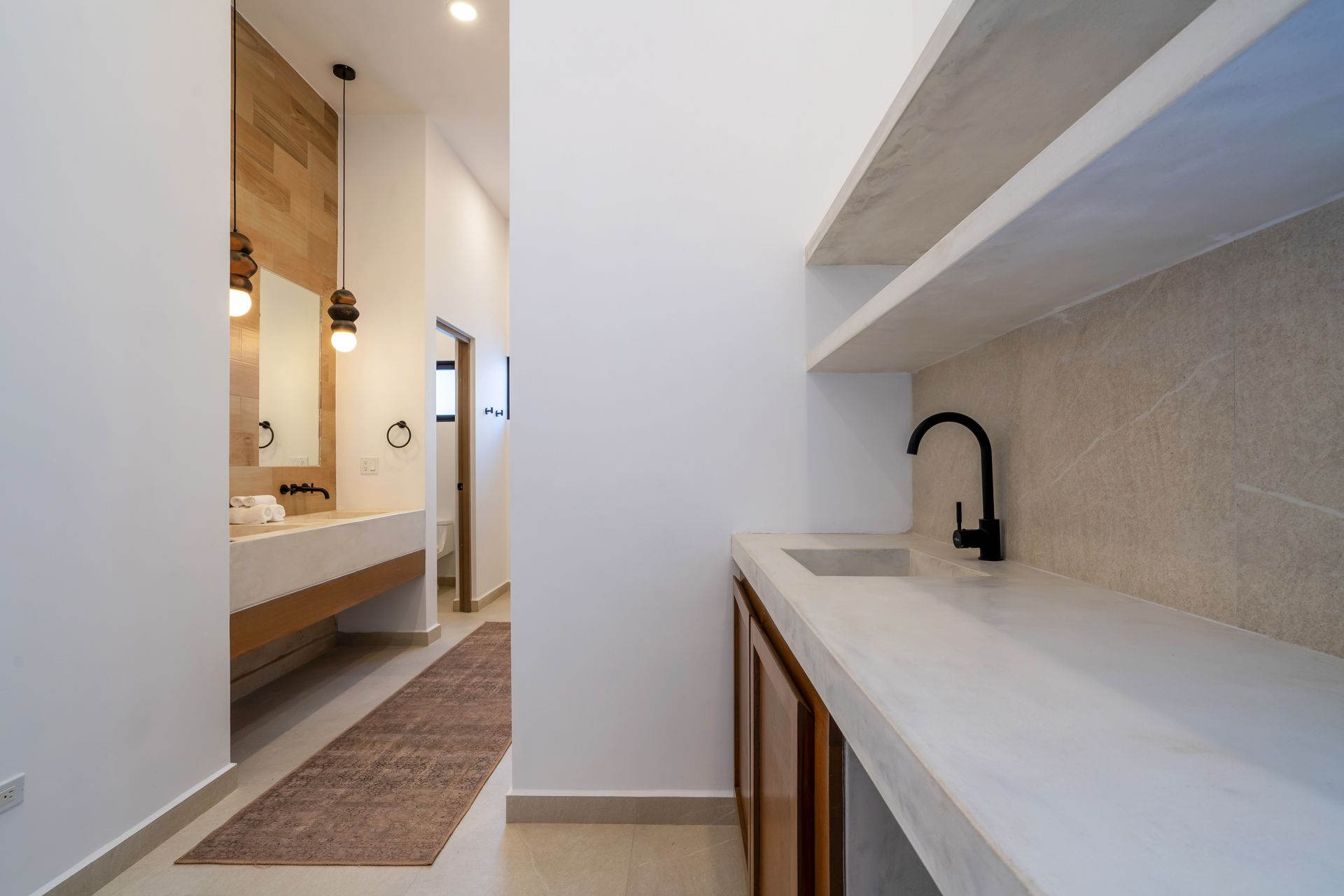 Modern bathroom with white walls, stone counters, wooden cabinetry, and a black faucet in a minimalist space.