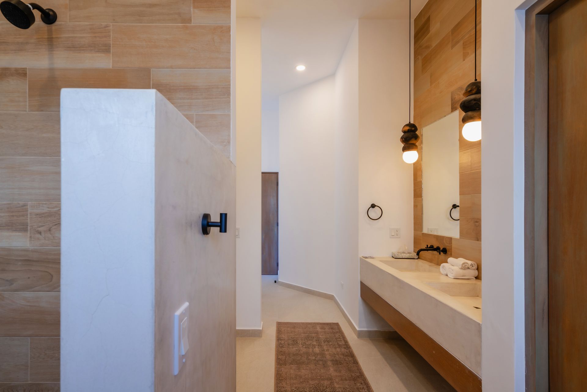 A modern bathroom with wood-look tile walls, a floating concrete vanity, dual pendant lights, and a towel hook.