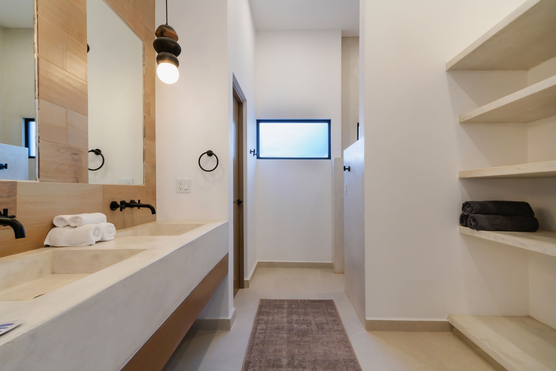 Modern minimalist bathroom featuring a double vanity, a beige concrete countertop, floating shelves, and warm lighting.