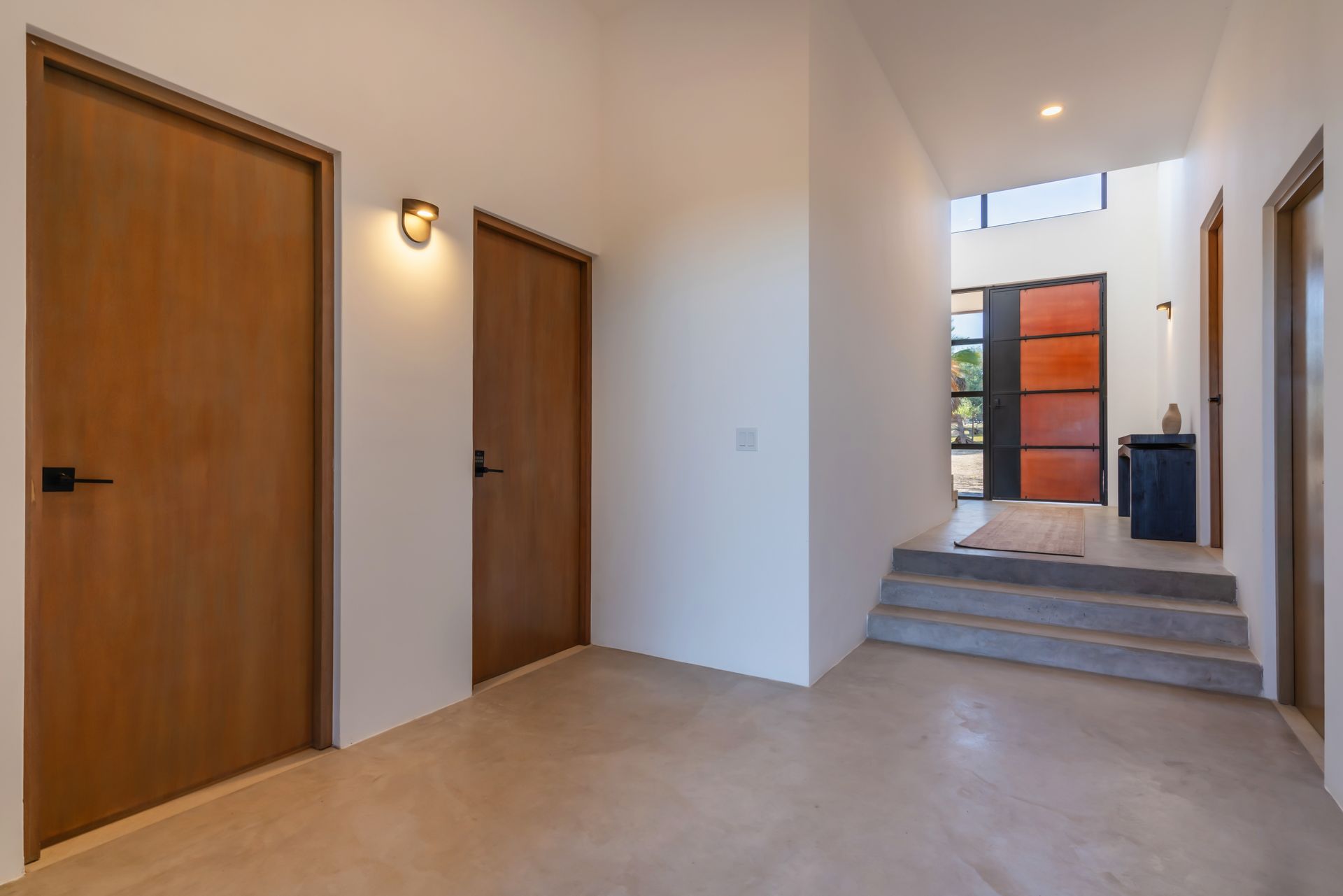 A modern home interior with smooth floors, white walls, wood doors, and steps leading to a glass entrance door.