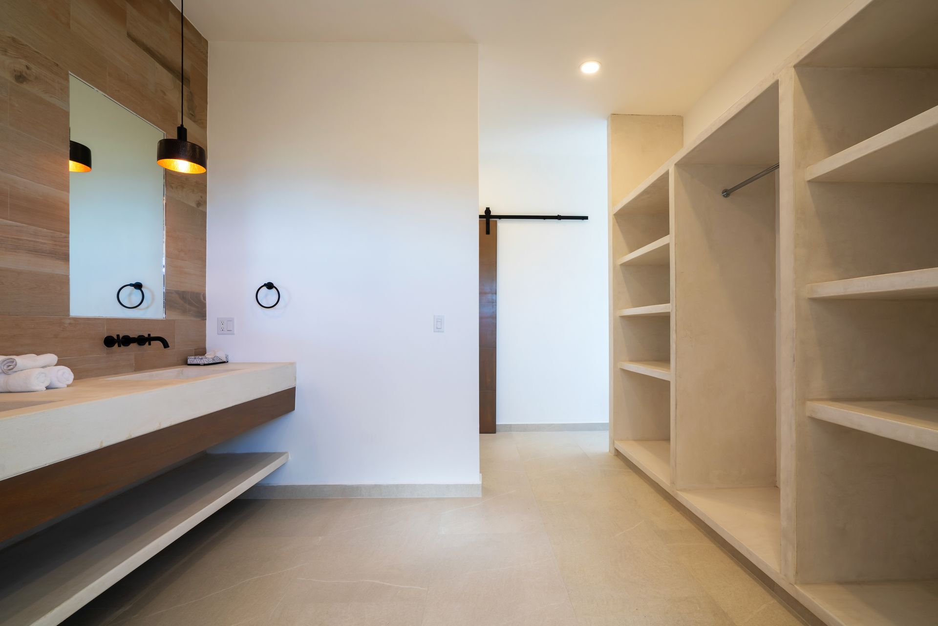 A modern bathroom featuring a floating concrete vanity with wood accents and a walk-in closet with built-in white shelves.