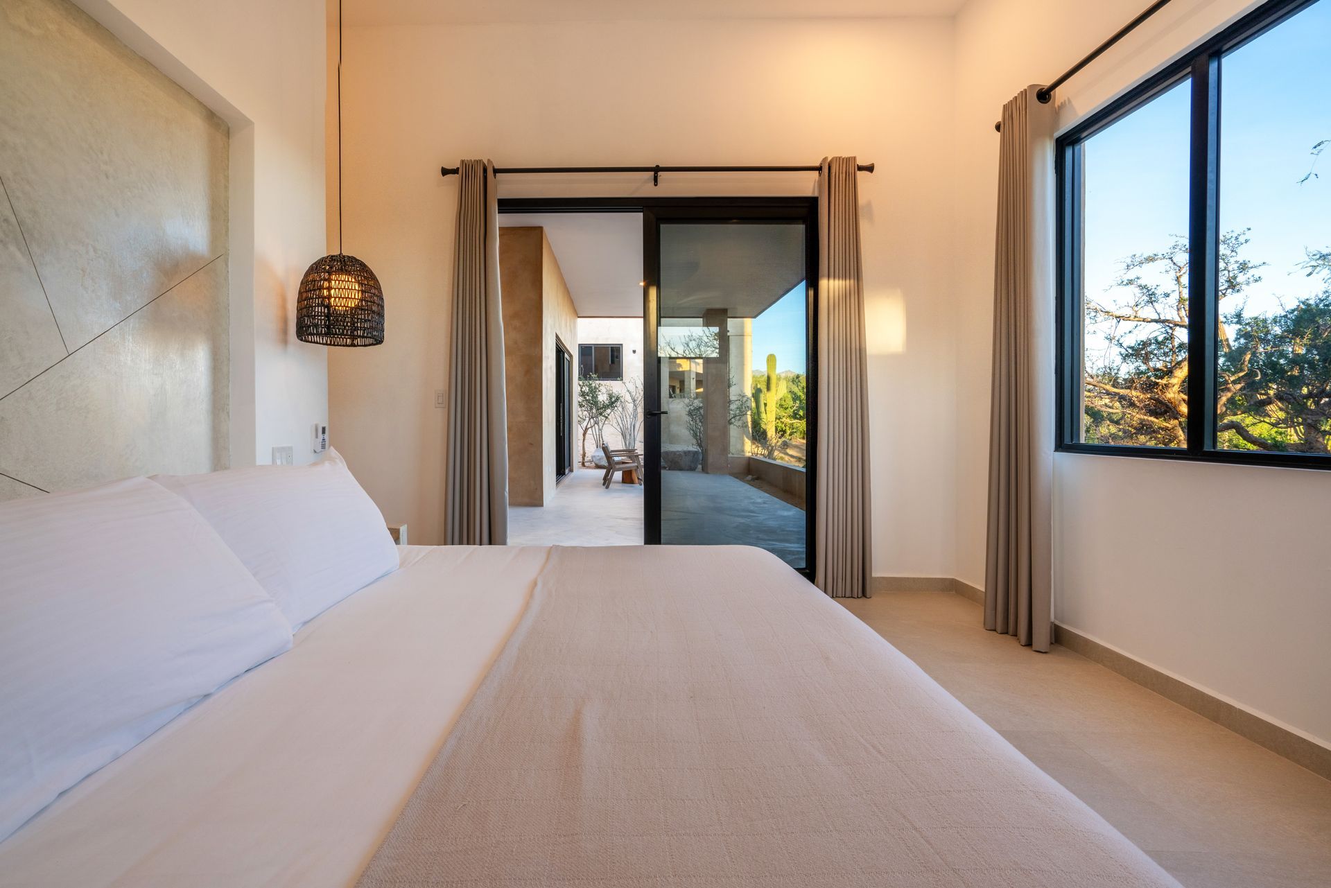 A hotel bedroom featuring a bed with white linens, a hanging lantern, sliding glass doors, and a sunny outdoor view.