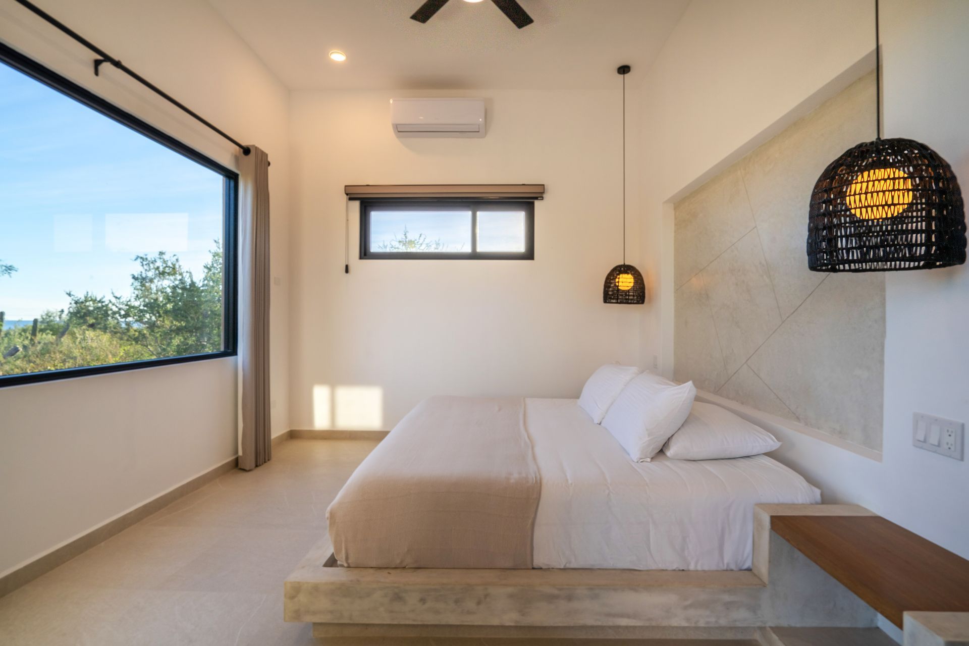 Modern hotel bedroom with a platform bed, large panoramic window, white walls, and a hanging basket pendant light.