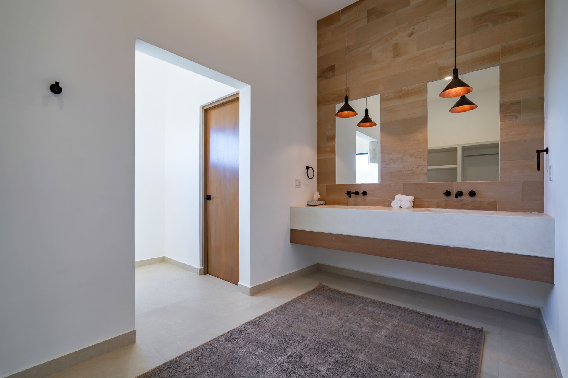A modern, minimalist bathroom with a floating concrete double vanity against a wood-paneled wall, dual mirrors, and rug.