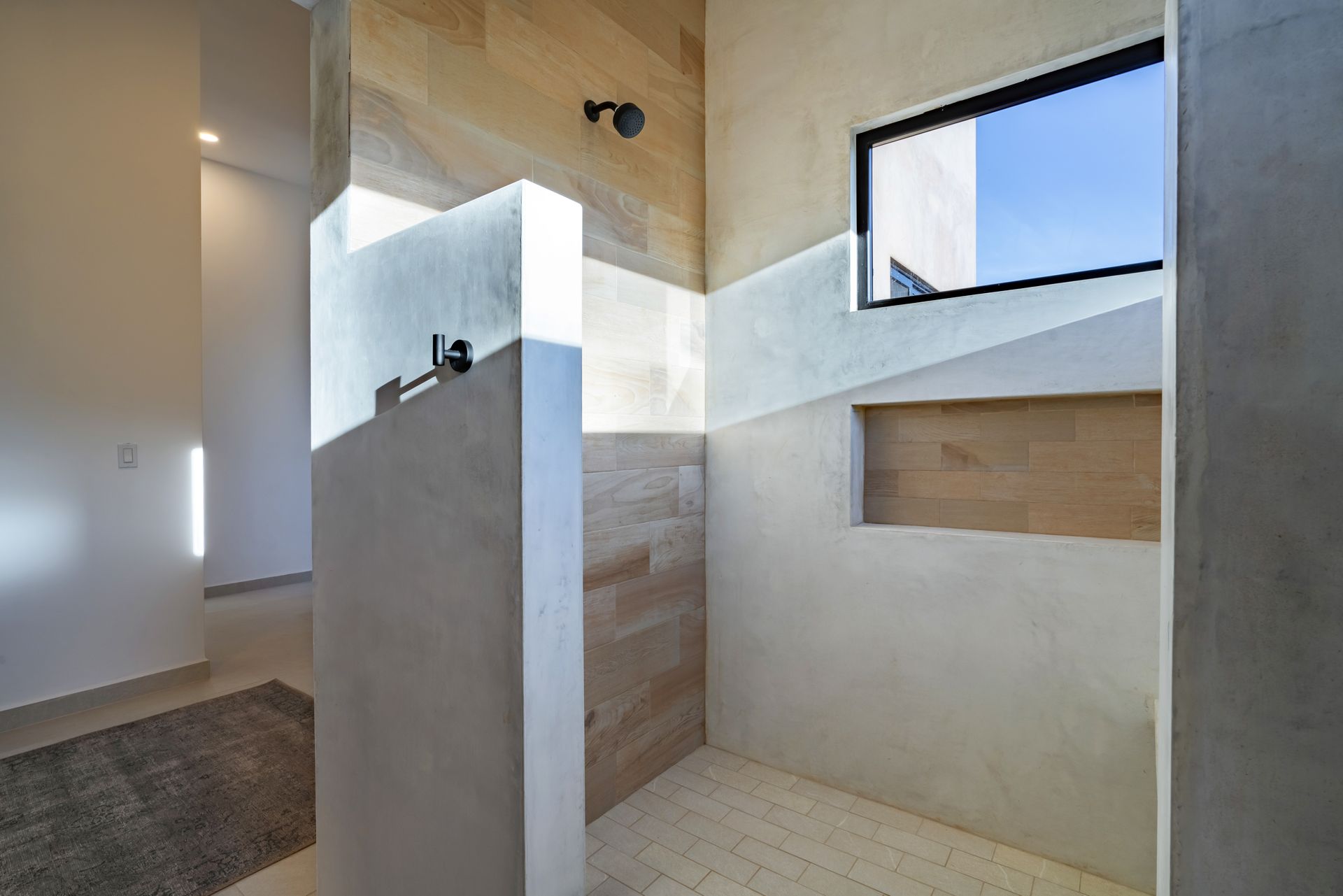 A modern, minimalist shower featuring concrete and wood-paneled walls, a built-in recessed niche, and a window.