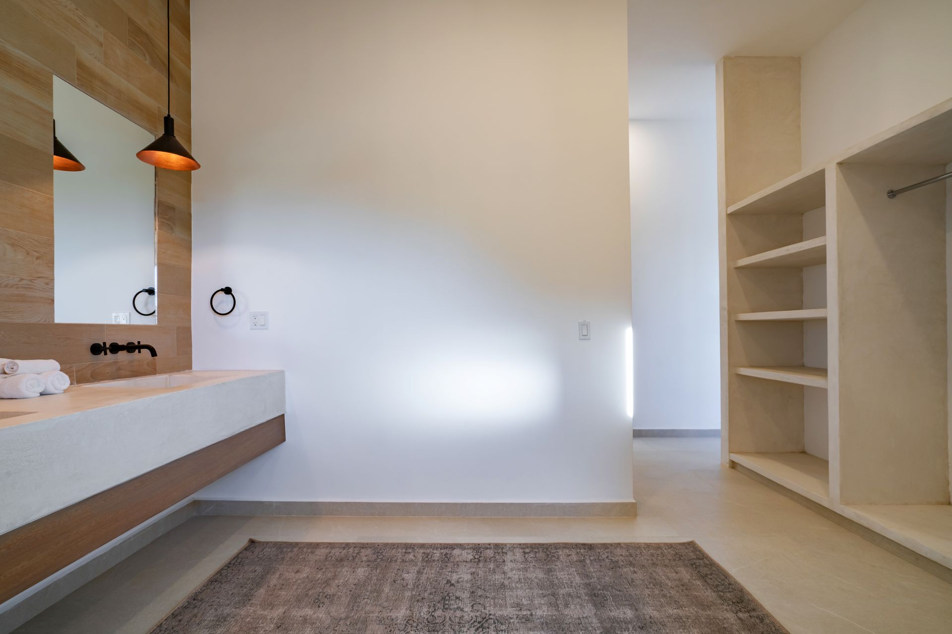 A modern bathroom with a wood-paneled wall, floating white vanity, rectangular mirror, pendant lighting, and shelving unit.