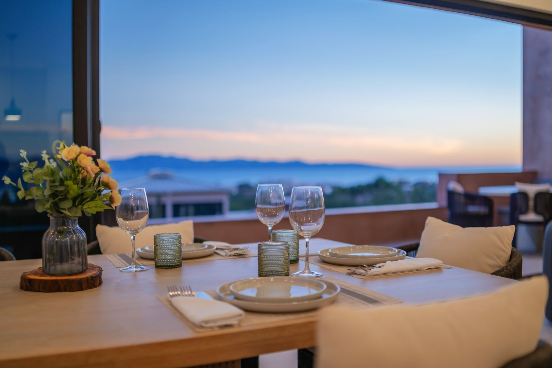 A dining table set for four on a terrace overlooking a scenic ocean horizon during sunset.