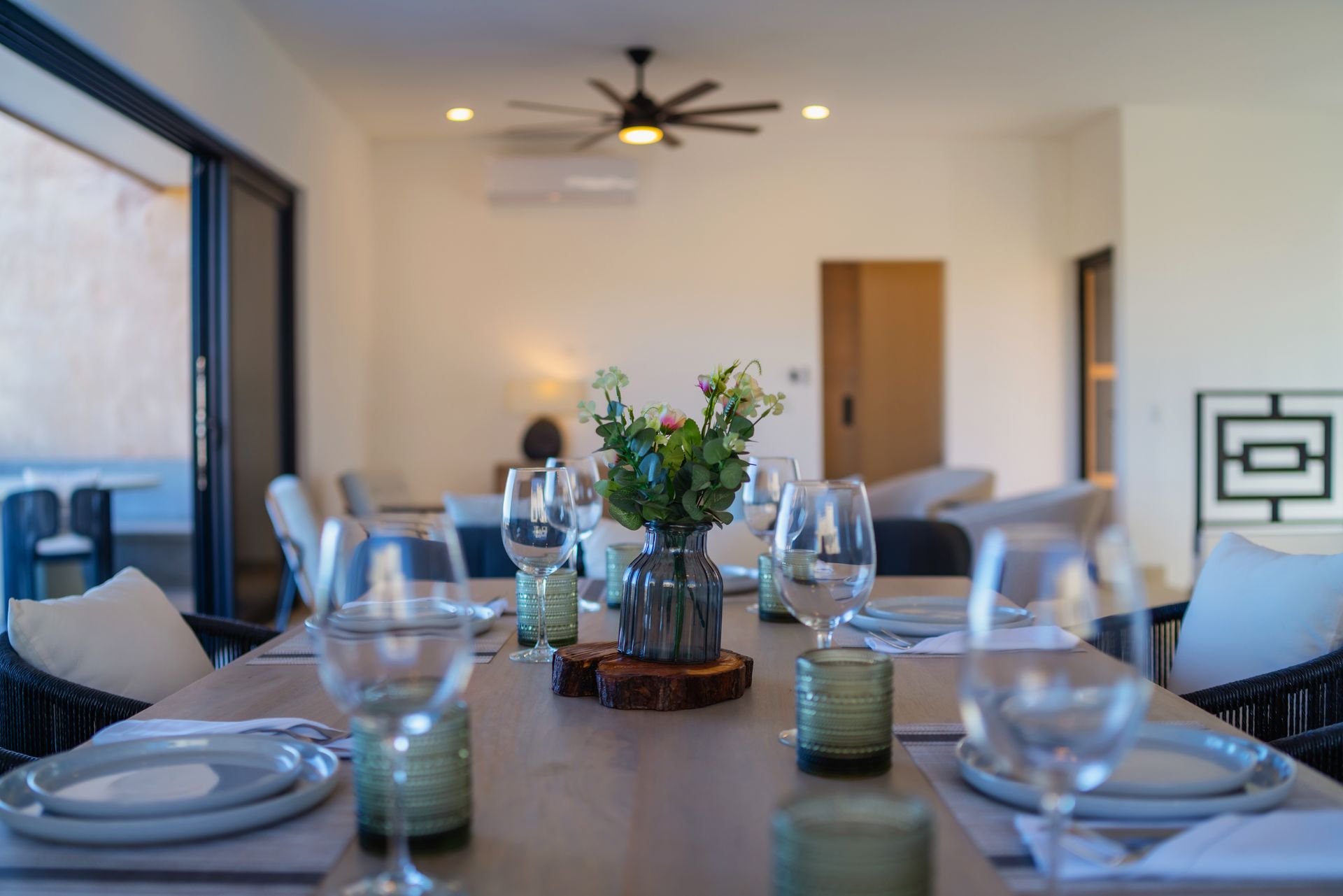 A dining table set for guests with wine glasses, plates, and a floral centerpiece in a bright, modern living space.