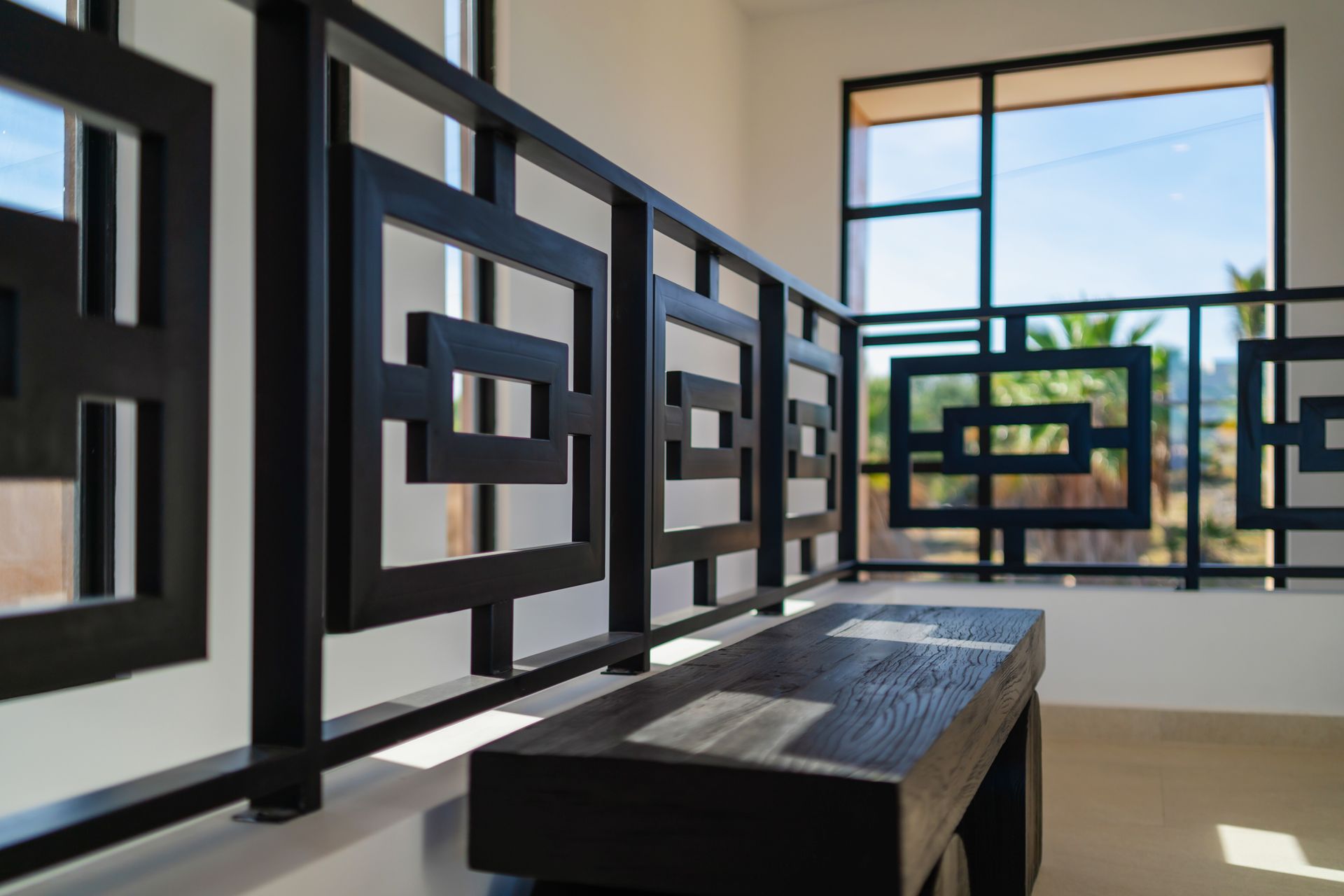A modern black wooden bench placed next to a geometric black railing in a bright, minimalist indoor space.
