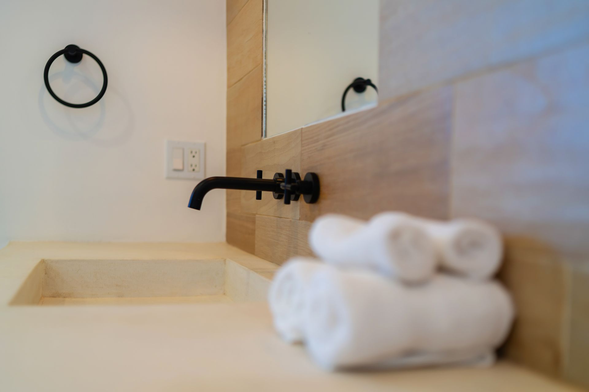 Modern bathroom sink with a stone countertop, matte black wall-mounted faucet, and stacked white towels.