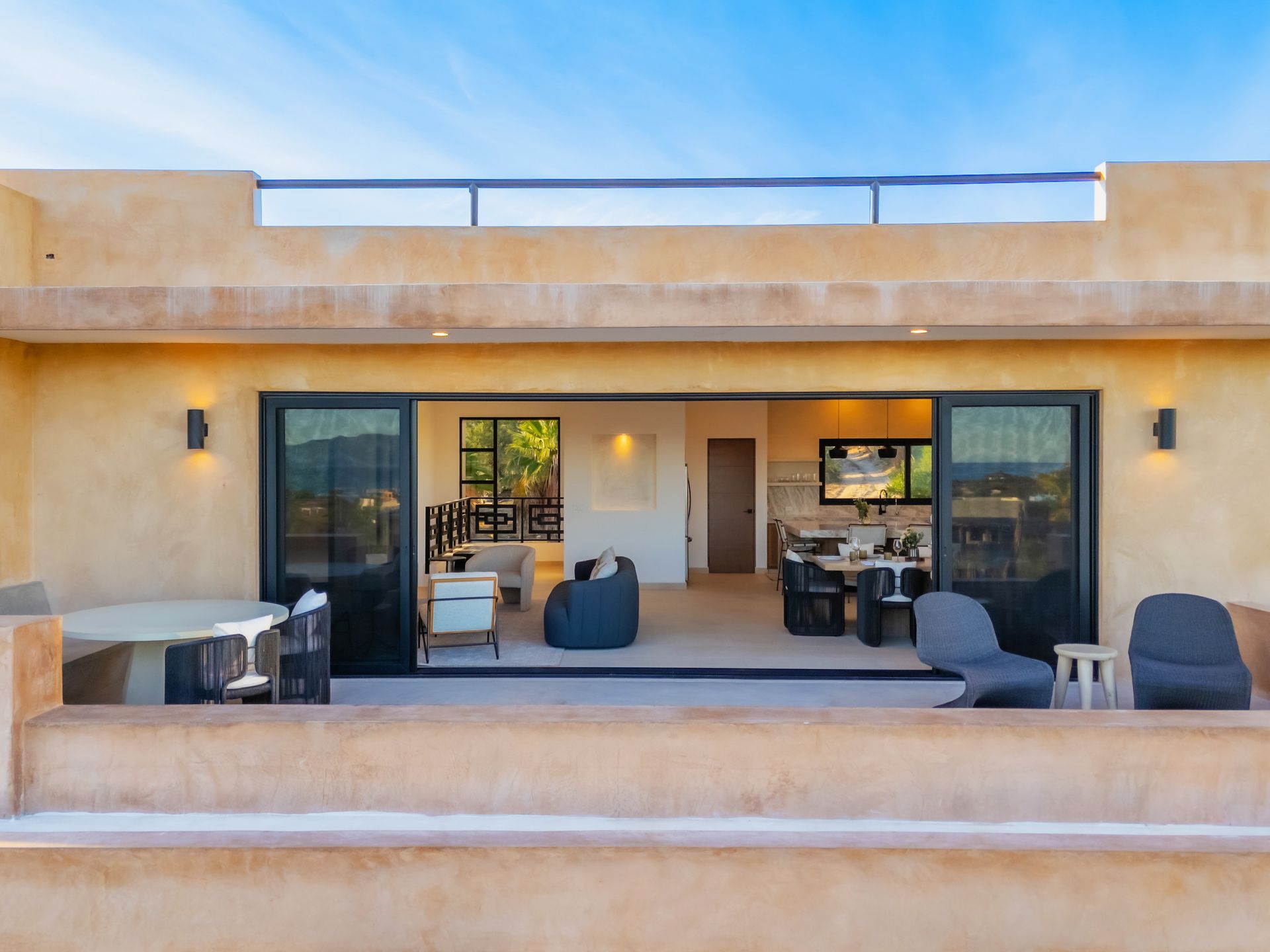 A patio view into a modern open-concept living area with earth-toned walls, dark furniture, and glass sliding doors.