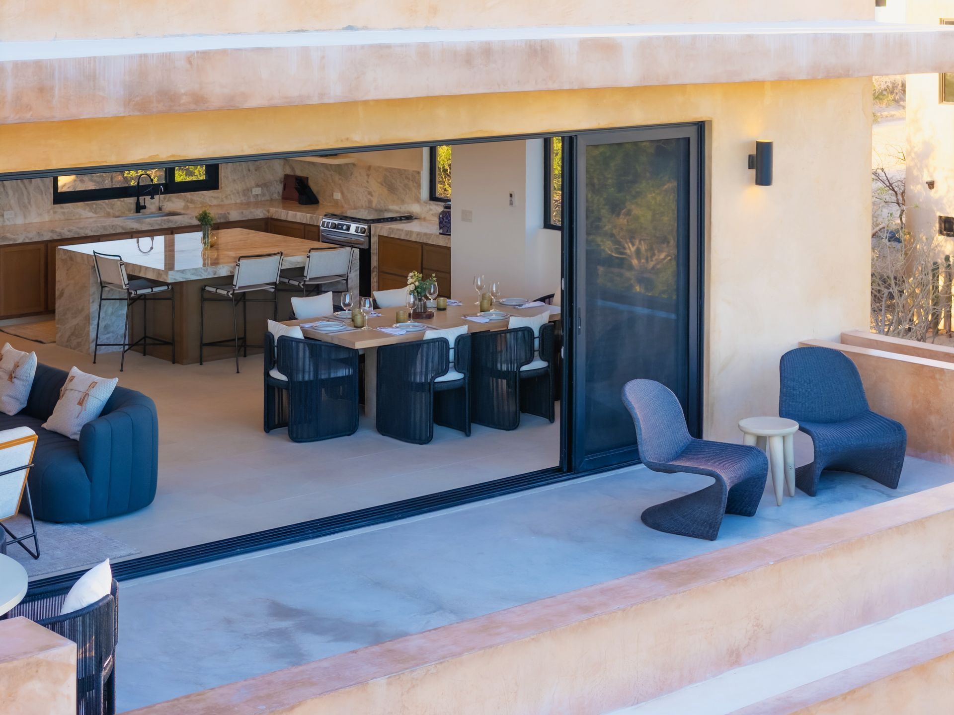 Modern open-plan home featuring an indoor dining area connected to an outdoor patio with blue chairs.