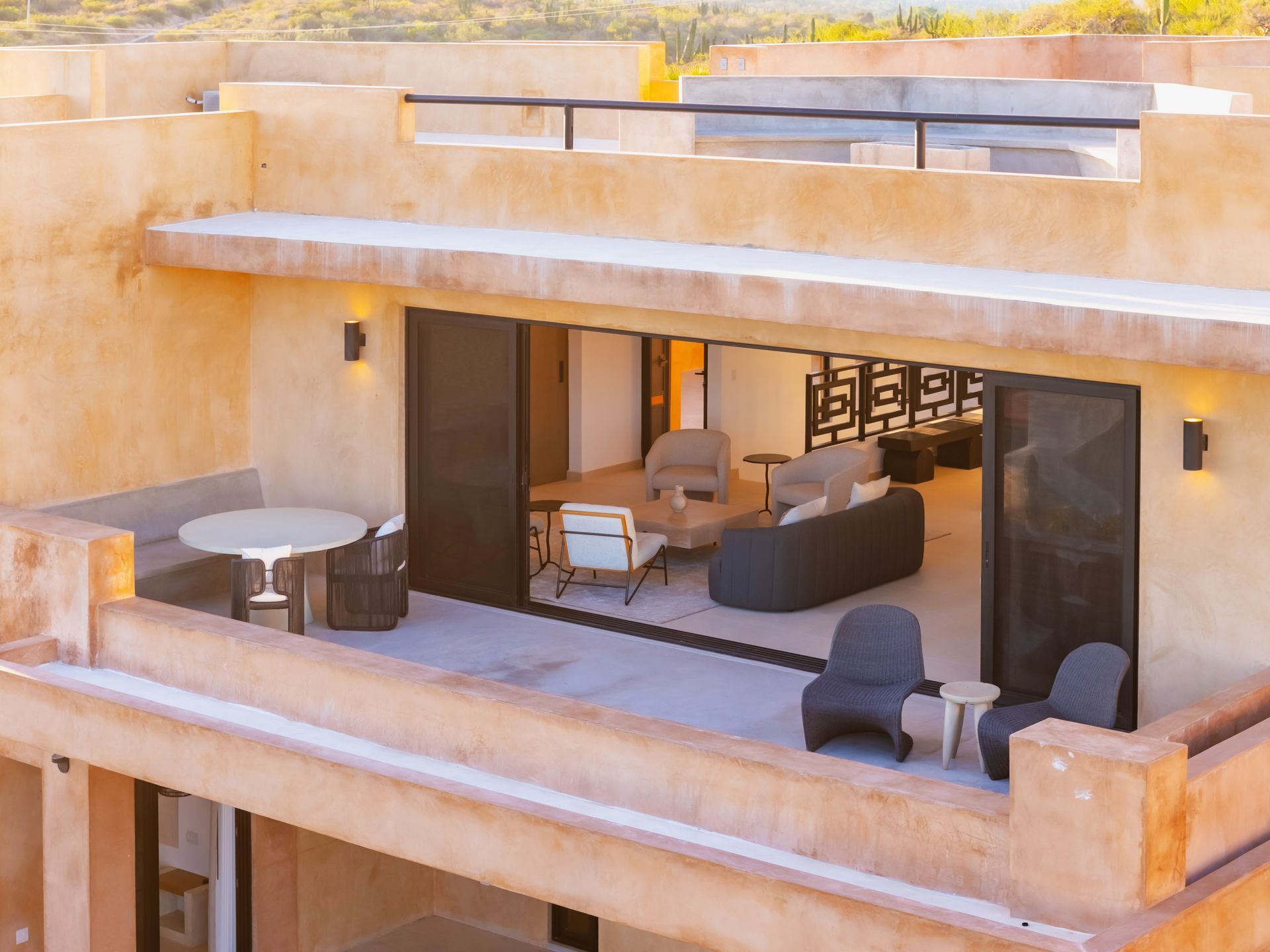 An elevated view of a modern terrace with neutral-toned walls, outdoor seating, and an open entryway into a living area.