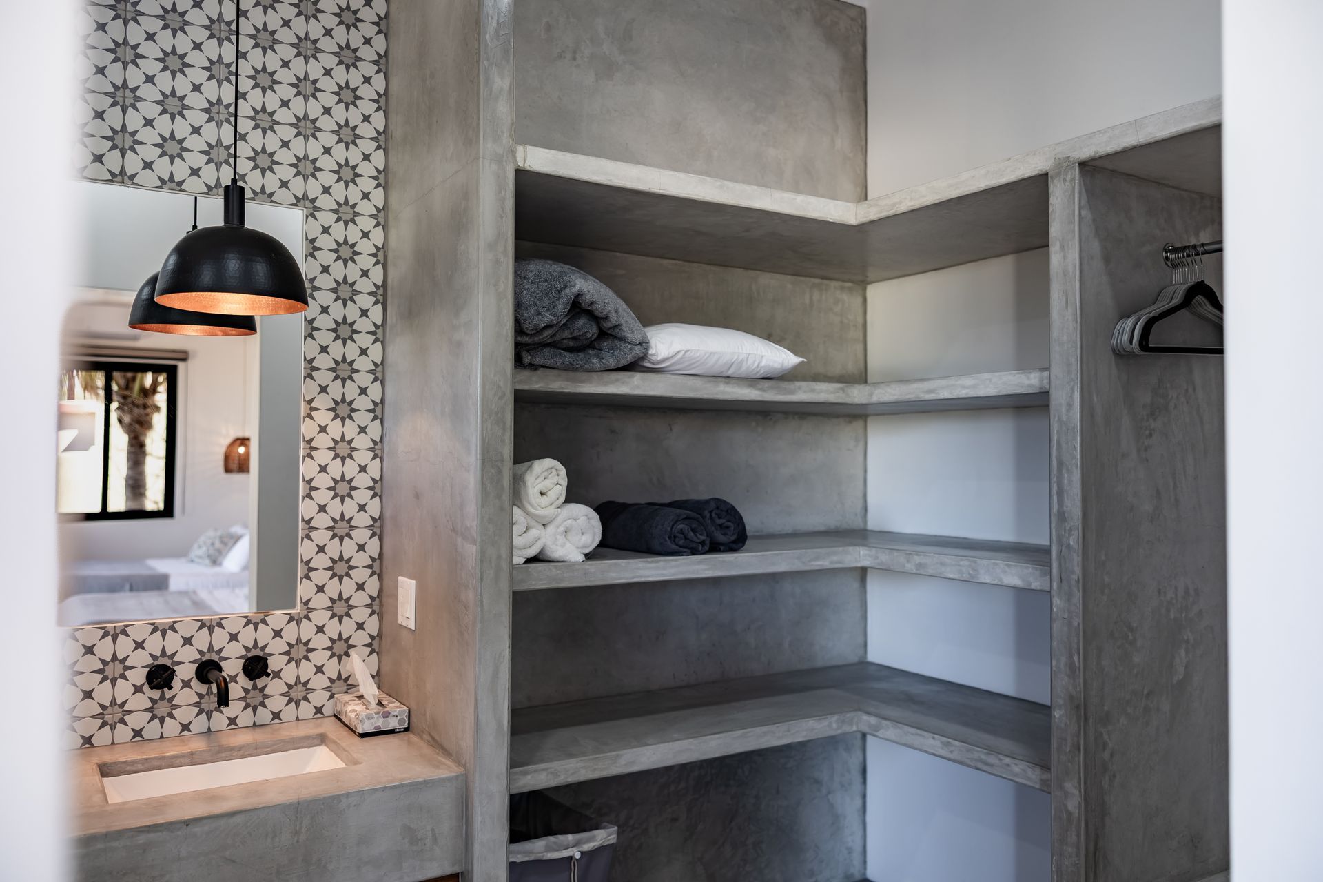 A modern bathroom vanity with a concrete sink and tiled wall, next to open concrete shelving holding towels and linens.