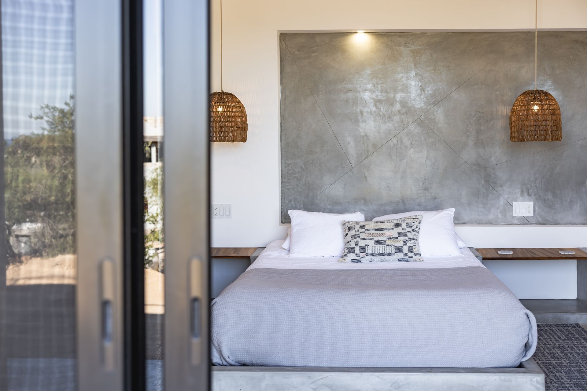 A bedroom featuring a bed with white pillows and a gray throw, set against a textured gray accent wall with woven lights.