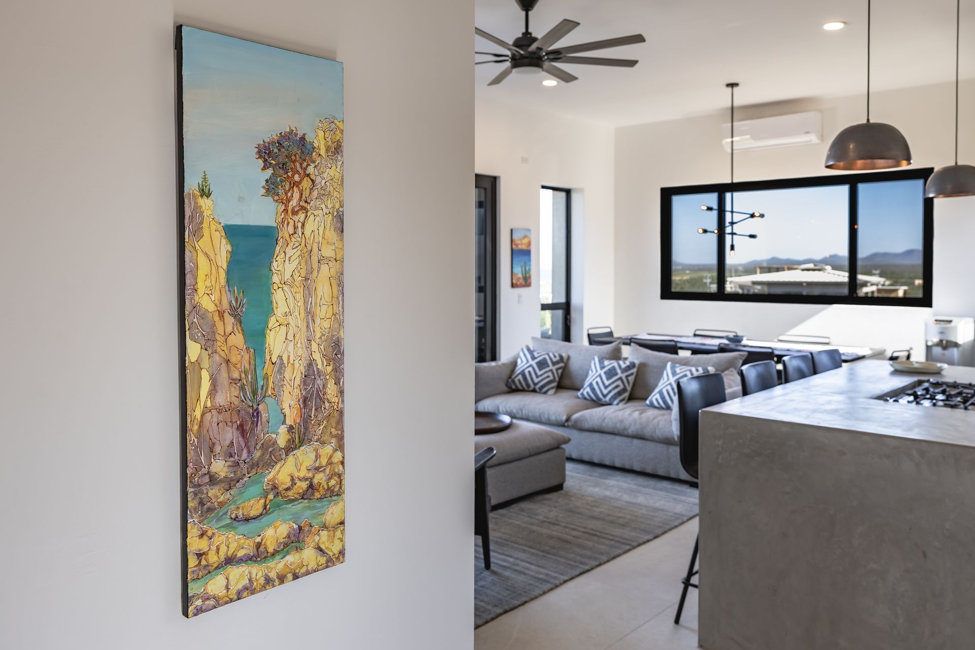 A tall landscape painting hangs on a white wall in the foreground, overlooking a modern open-plan living room.