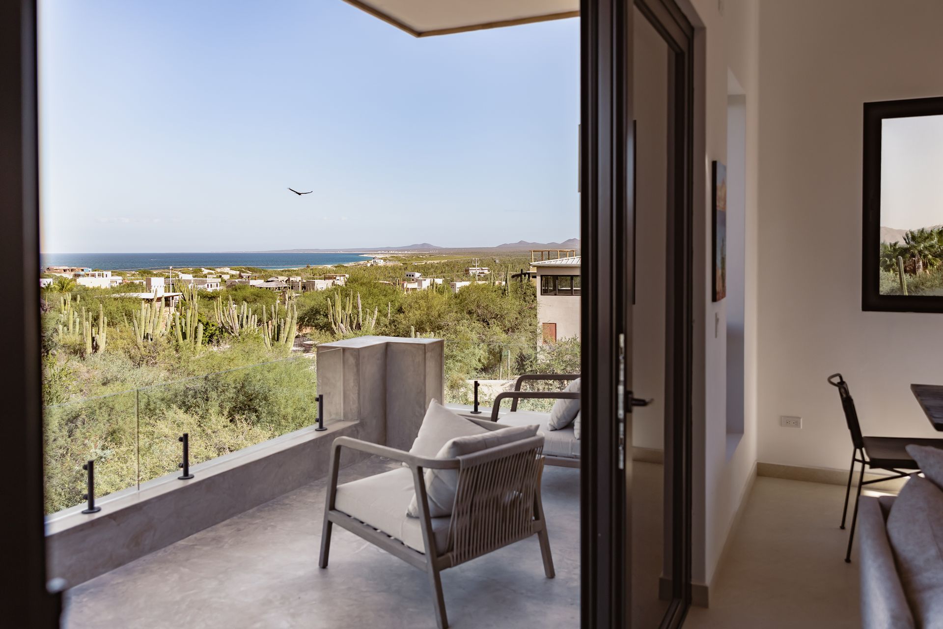 A balcony overlooking a lush landscape and the ocean, featuring modern outdoor chairs and a glass railing.