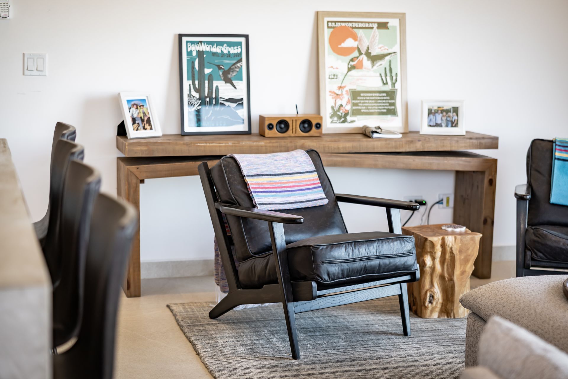 A black armchair with a striped throw sits on a rug before a wooden console table adorned with posters and decor.