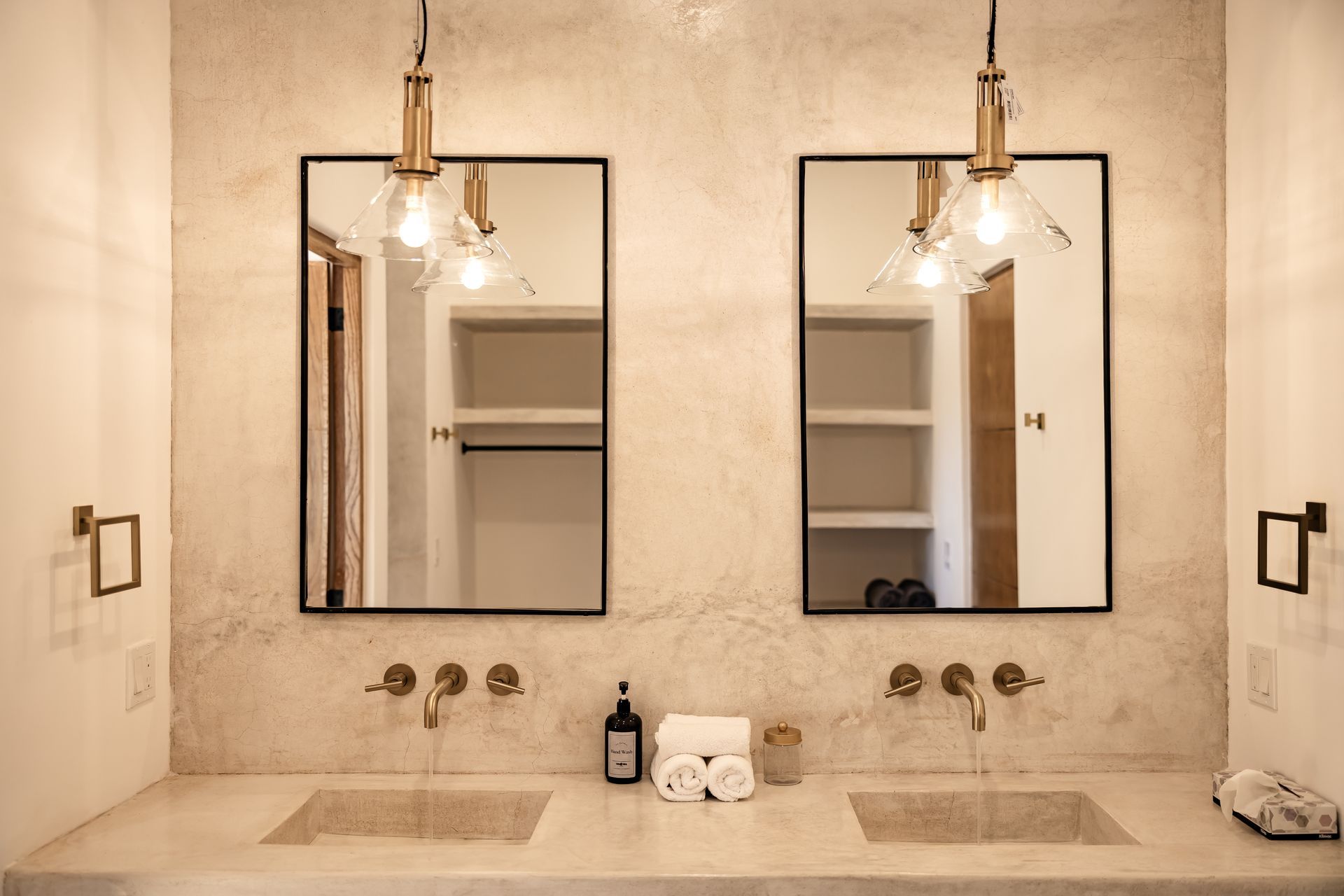 A double vanity bathroom with two mirrors, brass fixtures, pendant lights, and a stone countertop with white towels.