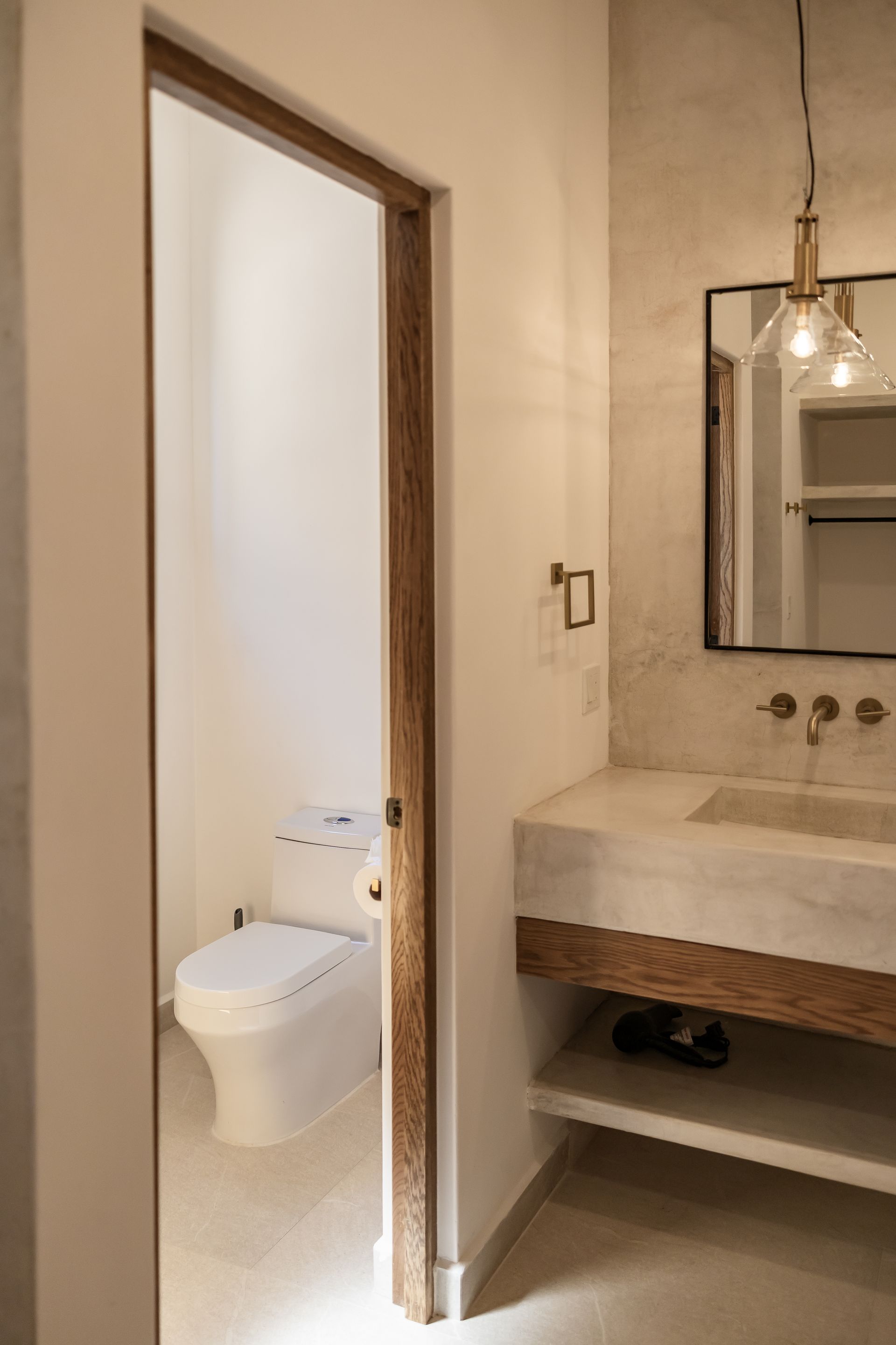 Modern bathroom with a marble sink, wood-trimmed floating vanity, pendant lighting, and an adjacent toilet room.