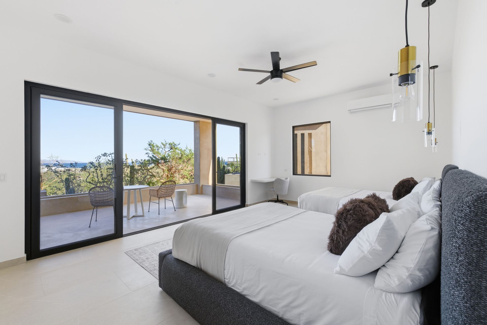 Modern hotel room with two beds, dark headboards, and large sliding glass doors opening to a scenic balcony view.