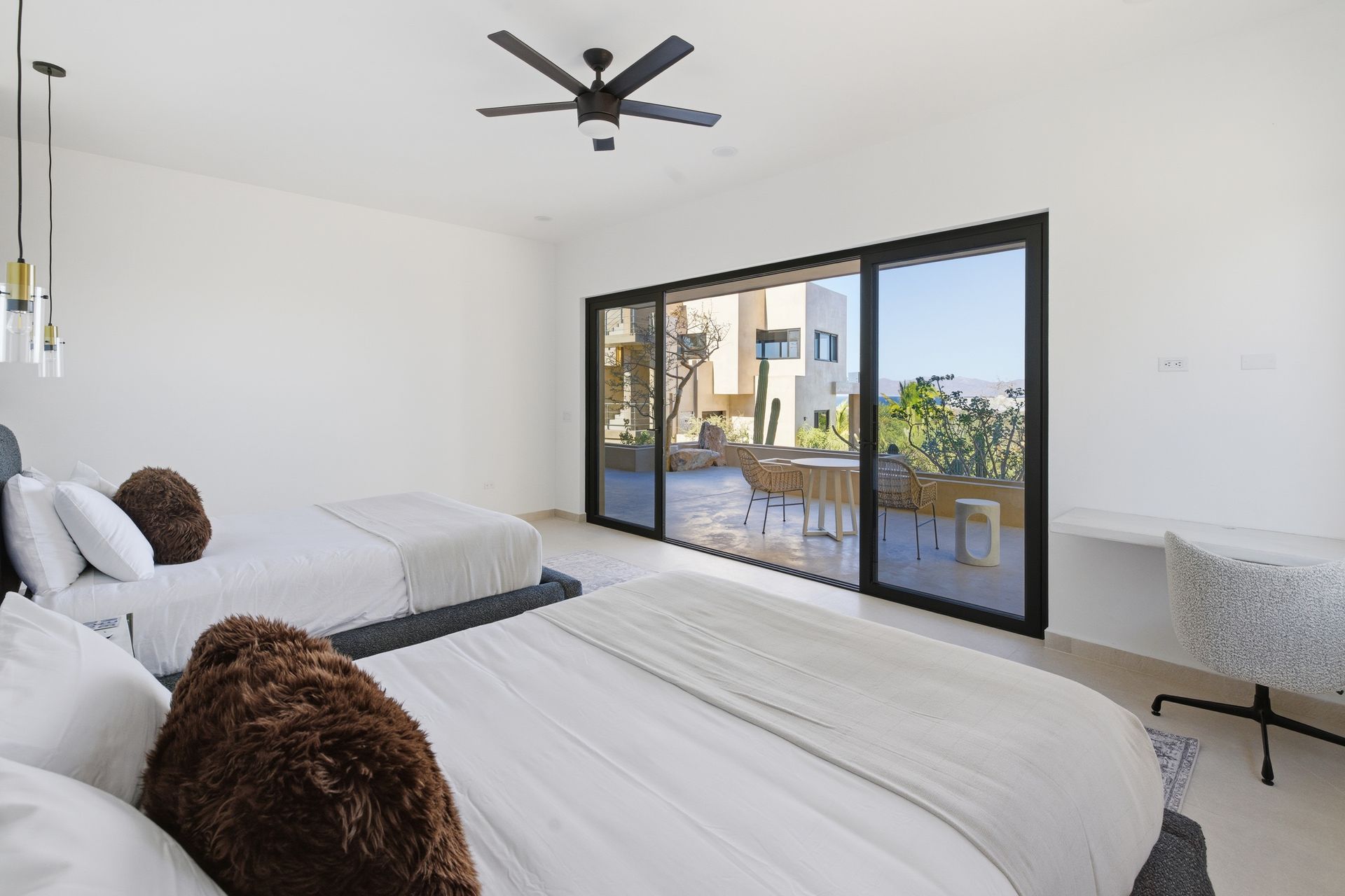A bright, modern bedroom with two queen beds, a ceiling fan, and sliding glass doors leading to a patio with a view.