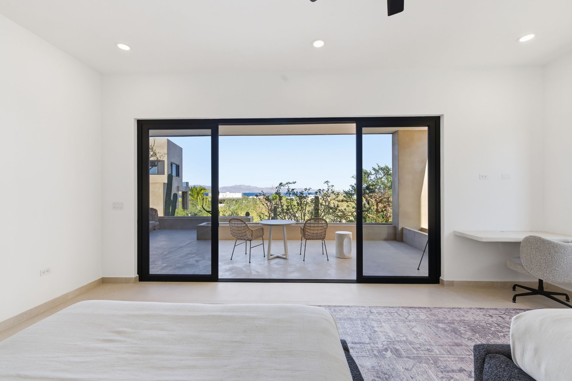 A bright room with white walls, a large sliding glass door to a patio with outdoor seating, and a desk area.