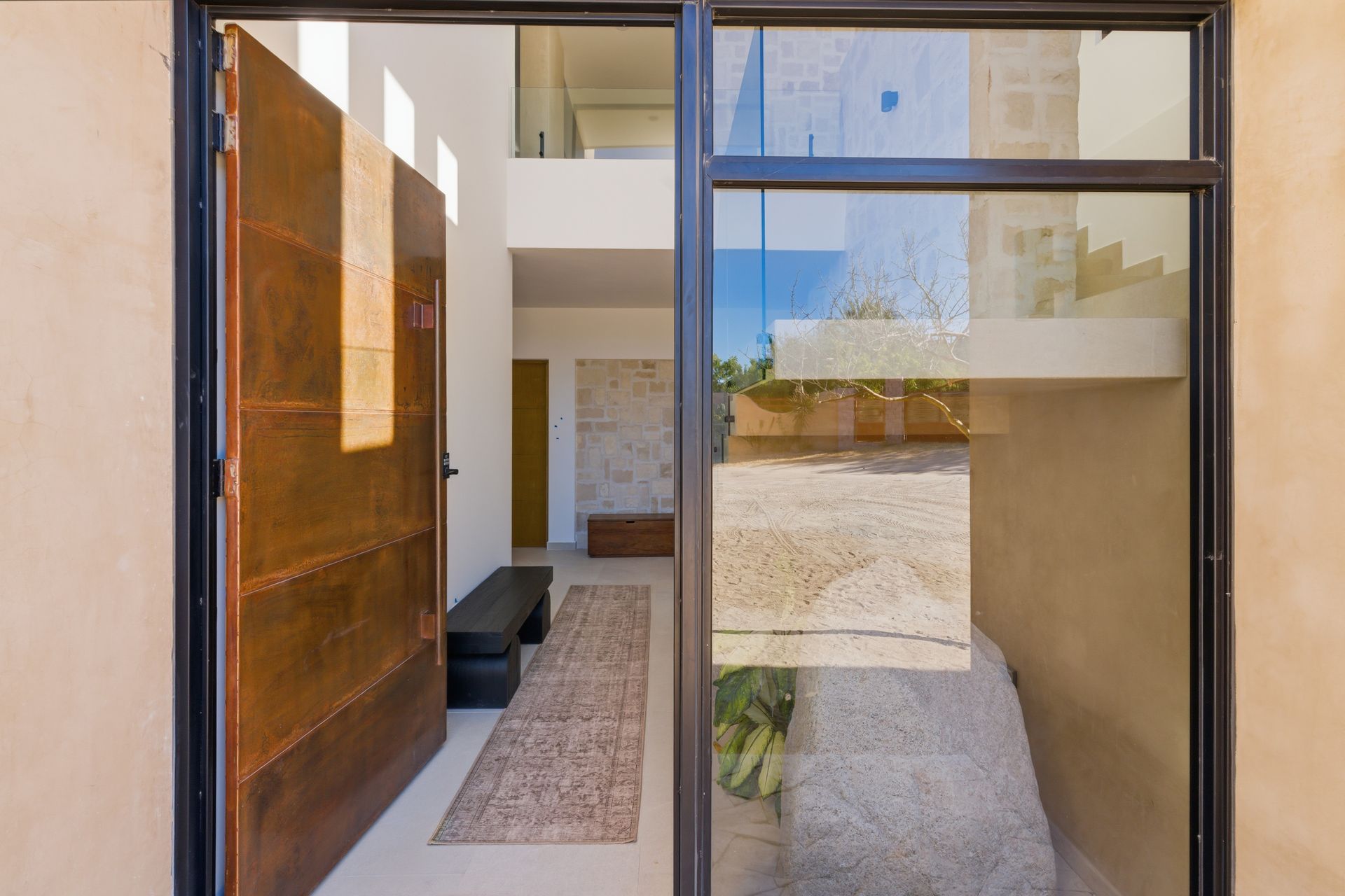 A modern entrance featuring a tall, rust-toned metal door, a long runner rug, and a glass-enclosed interior courtyard.