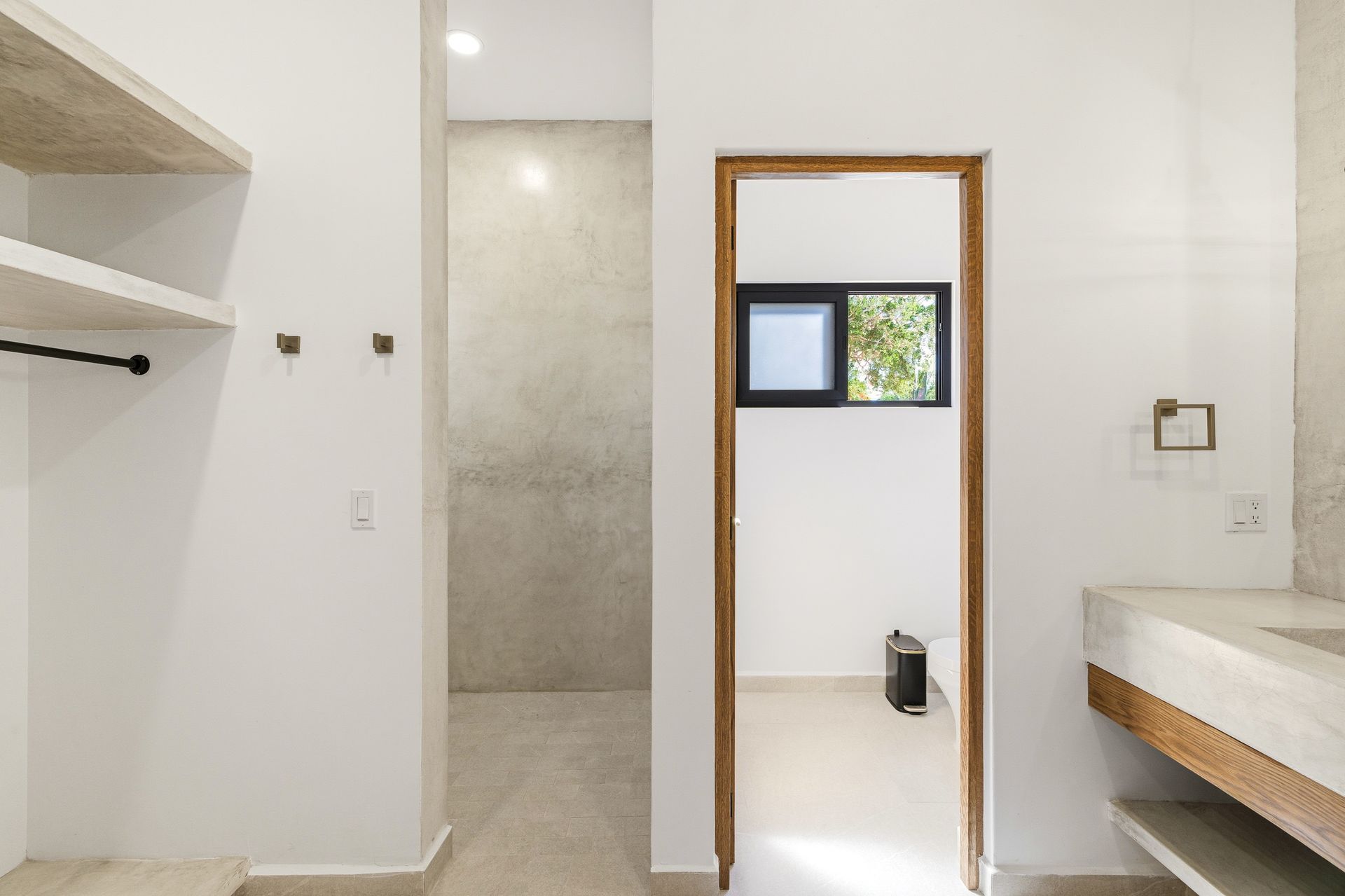 A modern bathroom with white walls, a stone-tiled shower area, a wooden doorway, and a floating vanity counter.