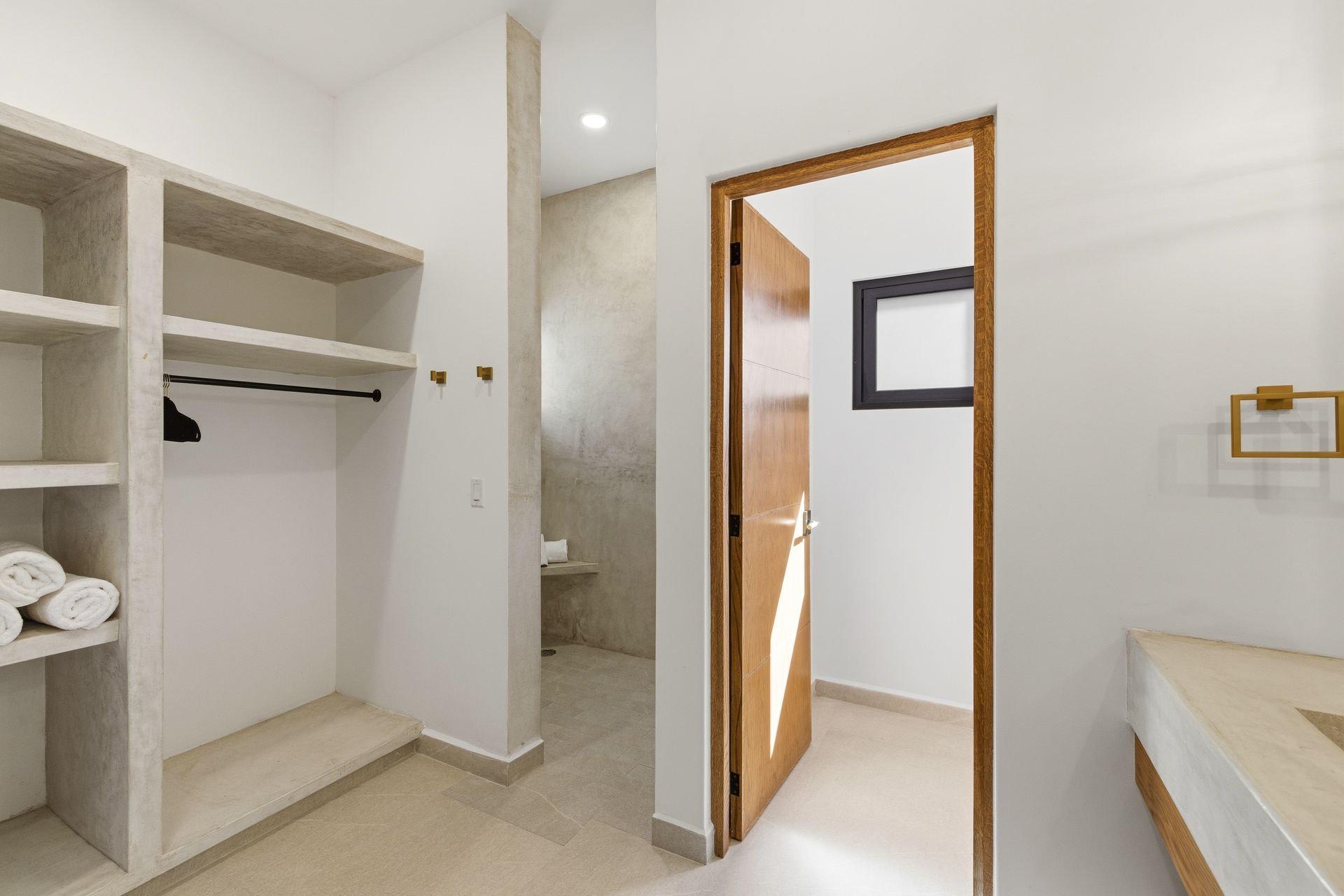 Modern walk-in closet with built-in shelves and hanging space leading to a bathroom doorway with white walls.