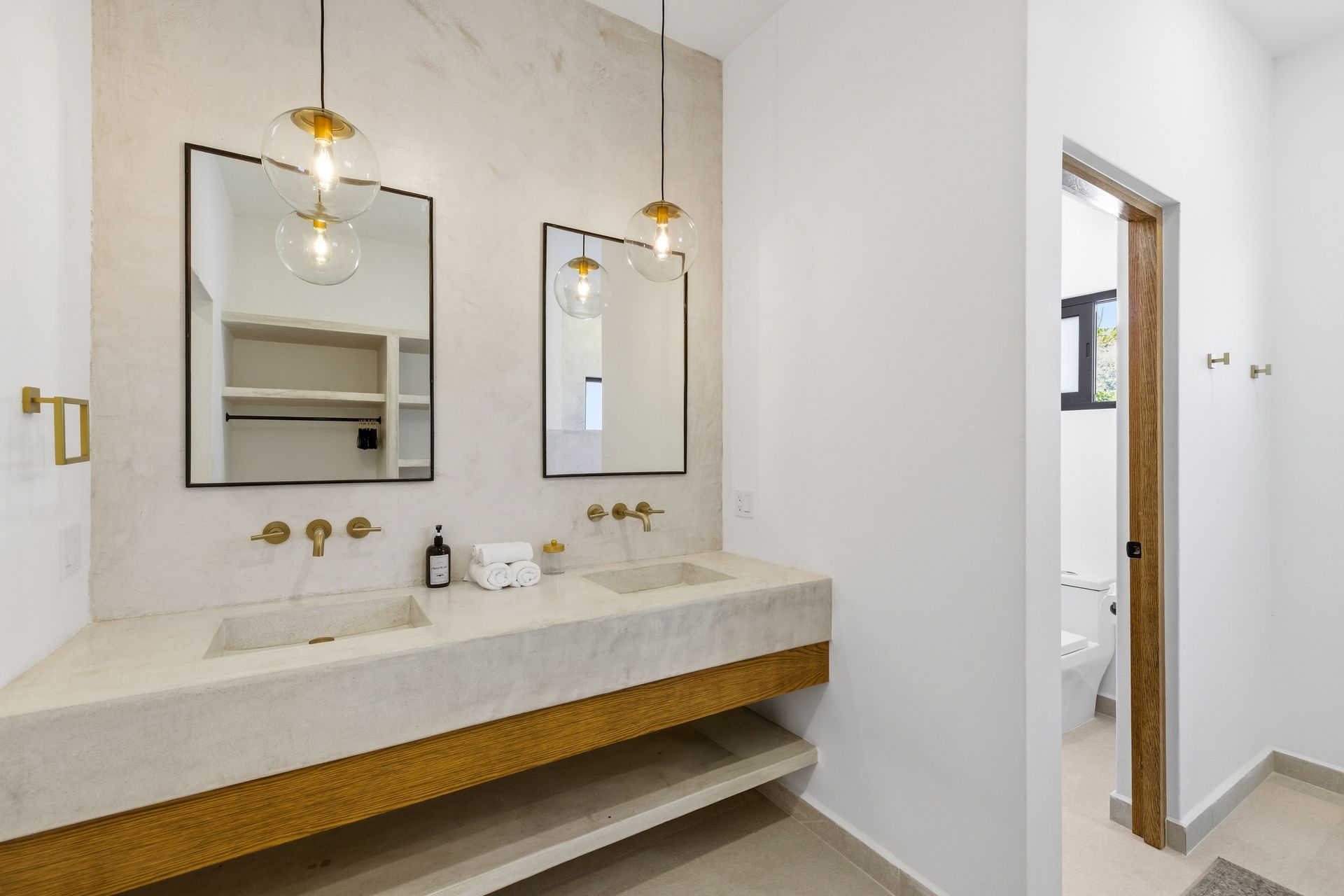 A modern bathroom with a double vanity, marble-style countertop, gold fixtures, hanging globe lights, and two mirrors.